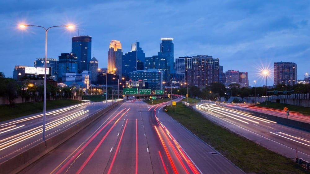 Minneapolis 桌布 壁紙 — 長時間曝光捕捉到黃昏時分高速公路上汽車燈光的軌跡，背景是閃爍的城市天際線。