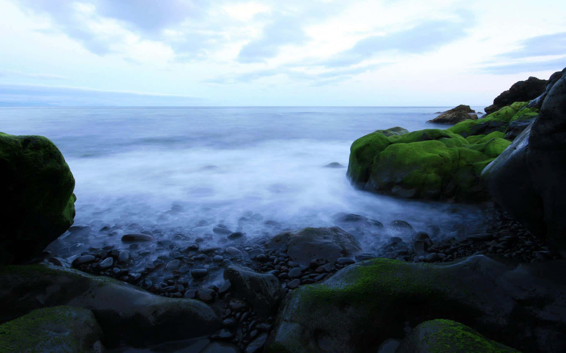 Relaxing 桌布 壁紙 — 長滿苔蘚的岩石在暮色中框住霧氣瀰漫的海洋，帶有柔和的藍色和綠色色調。