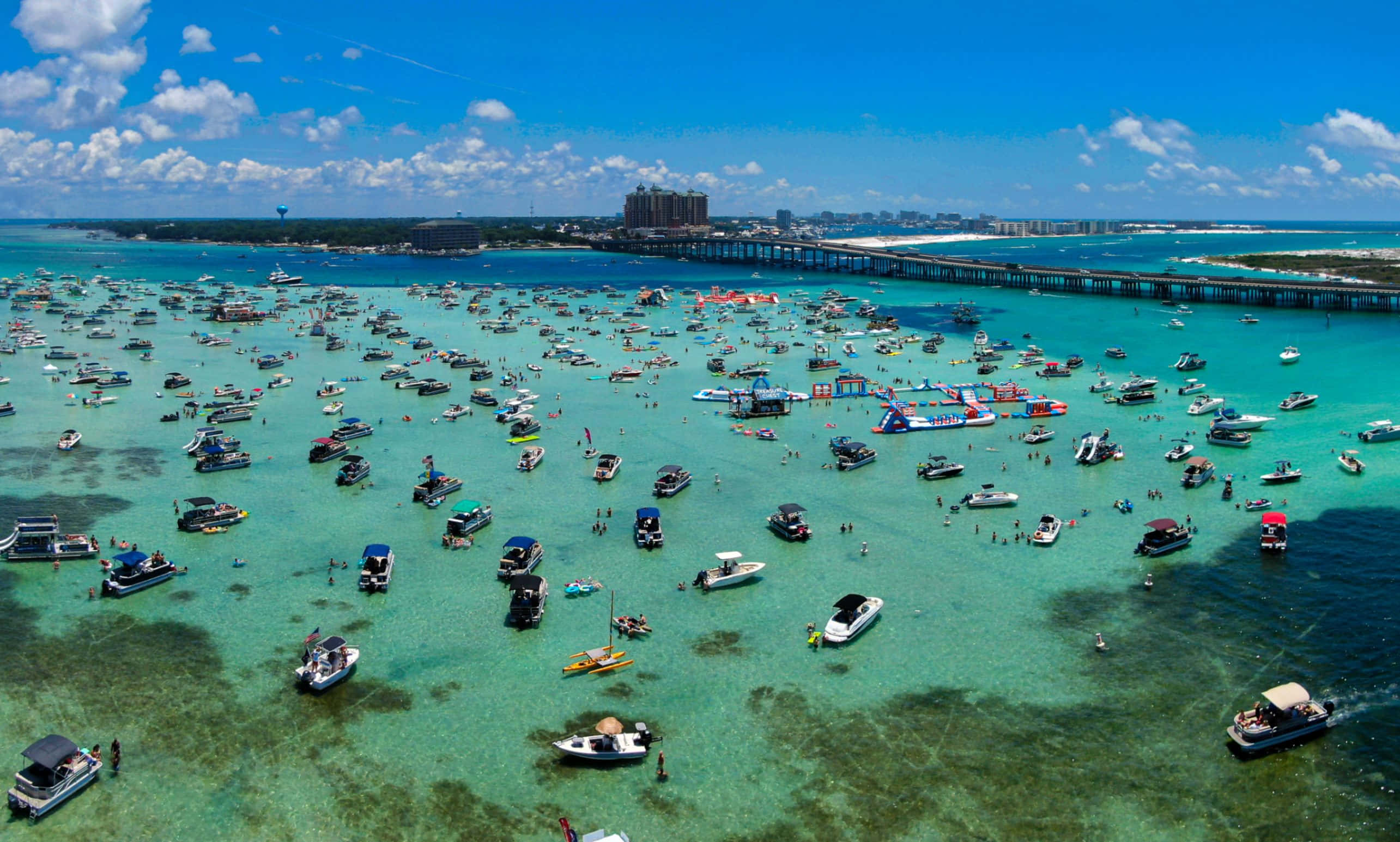 Crab Island 桌布 壁紙 — 長碼頭附近擠滿船隻和游泳者的碧綠海水鳥瞰圖，明亮的藍天白雲。
