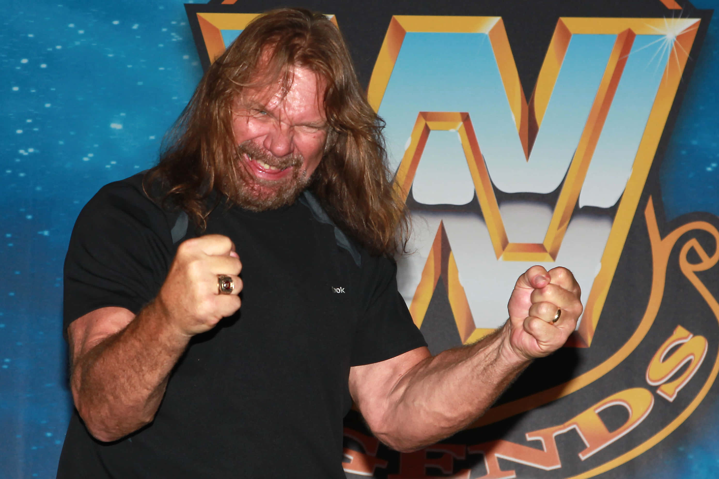 smiling 桌布 壁紙 — 長髮鬍鬚摔角手在WWE Legends標誌背景前揮舞拳頭。