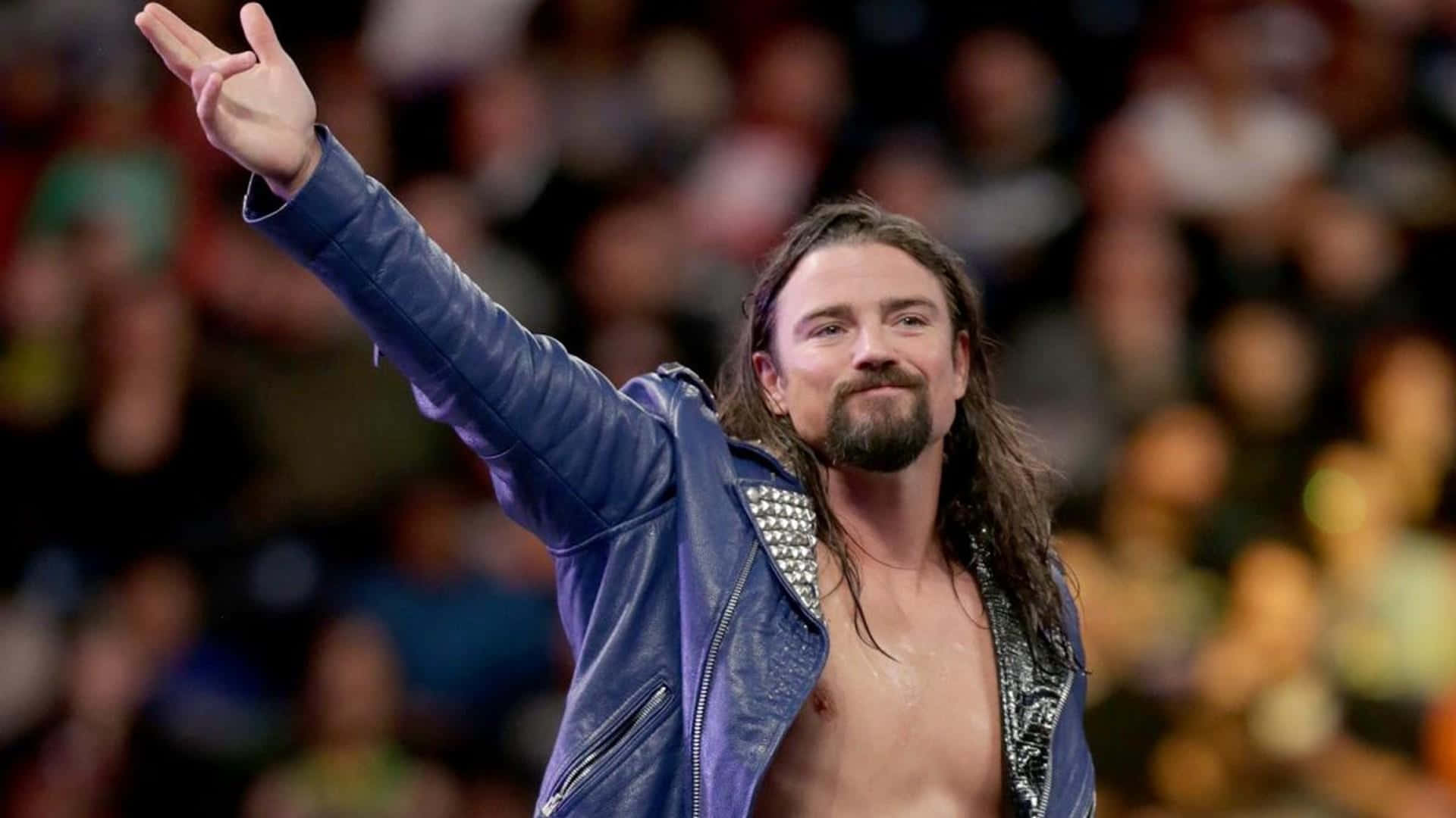 WWE 桌布 壁紙 — 長髮鬍鬚摔角手在現場活動中穿著藍色皮夾克向人群揮手。