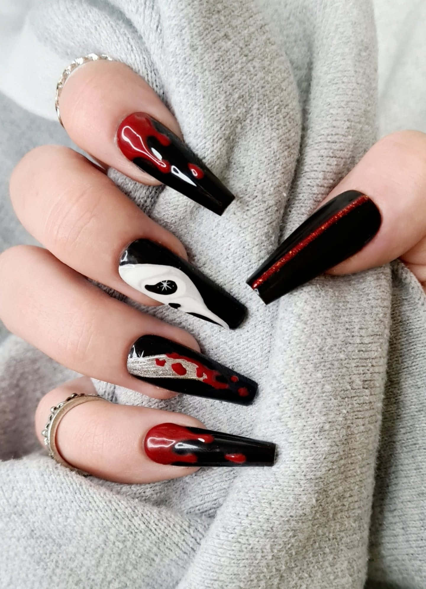 Halloween Nail Art 桌布 壁紙 — 長黑色細高跟指甲搭配紅色亮粉和血跡飛濺設計，放在柔軟的灰色毛衣袖子上。