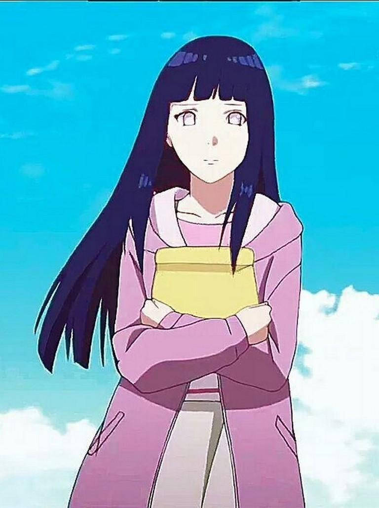 Hinata Hyuga 桌布 壁紙 — 長黑髮的動漫女孩穿著粉紅色連帽衫，拿著一本黃色書，背景是明亮的藍天和蓬鬆的雲朵。