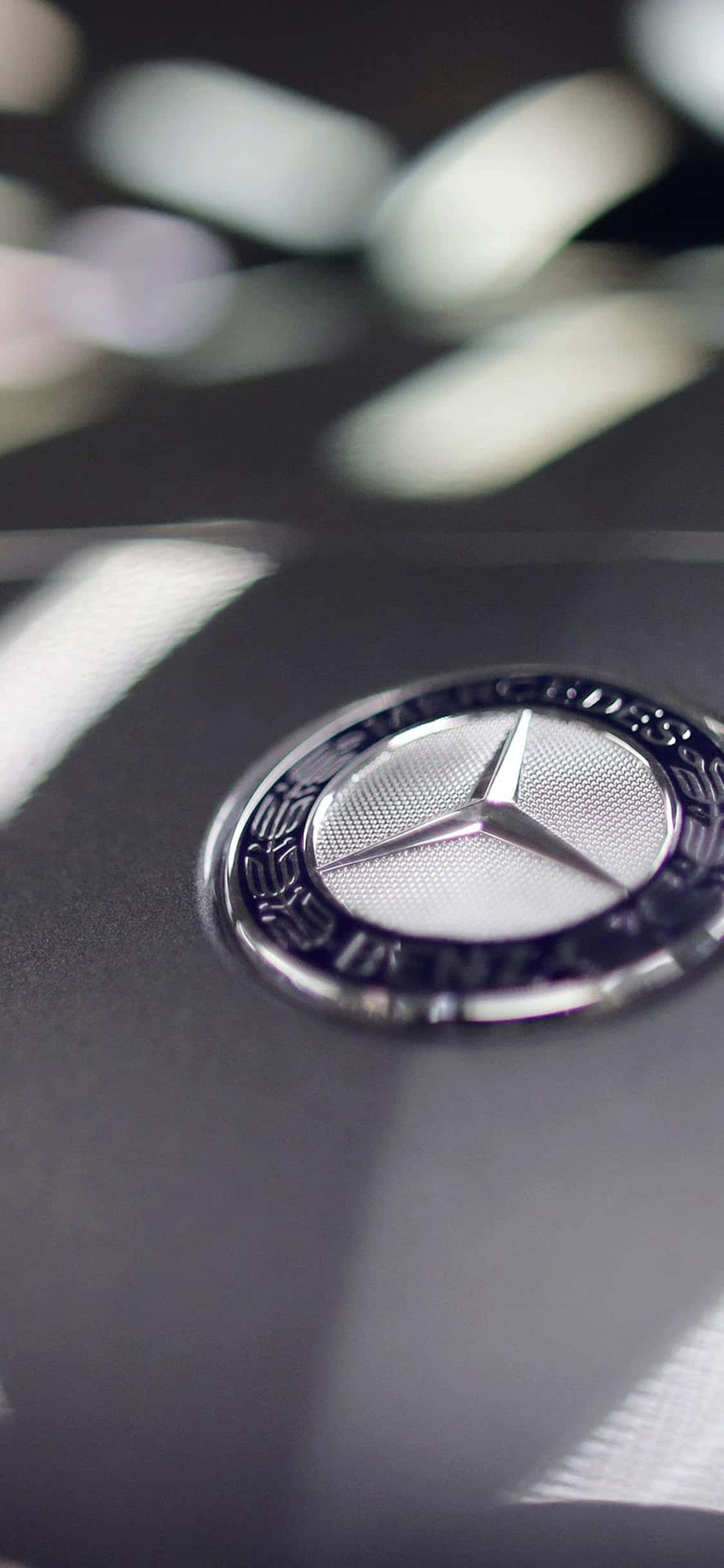 Mercedes 桌布 壁紙 — 閃亮 Mercedes-Benz 標誌的特寫，位於時尚黑色汽車引擎蓋上，帶有柔和的光線反射。