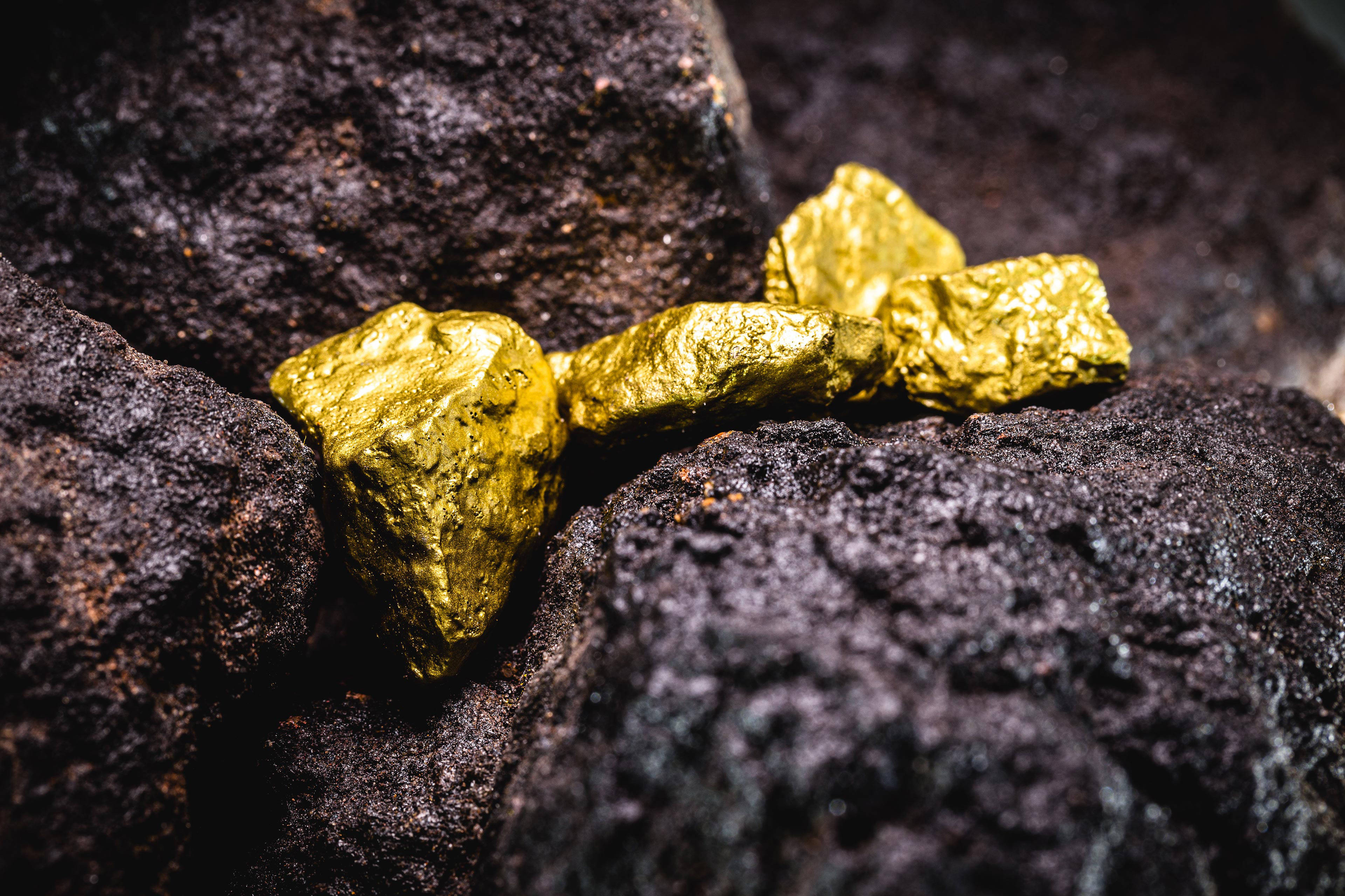 Stone 桌布 壁紙 — 閃亮不規則的金塊在暗色粗糙火山岩上閃耀，微距特寫鏡頭。