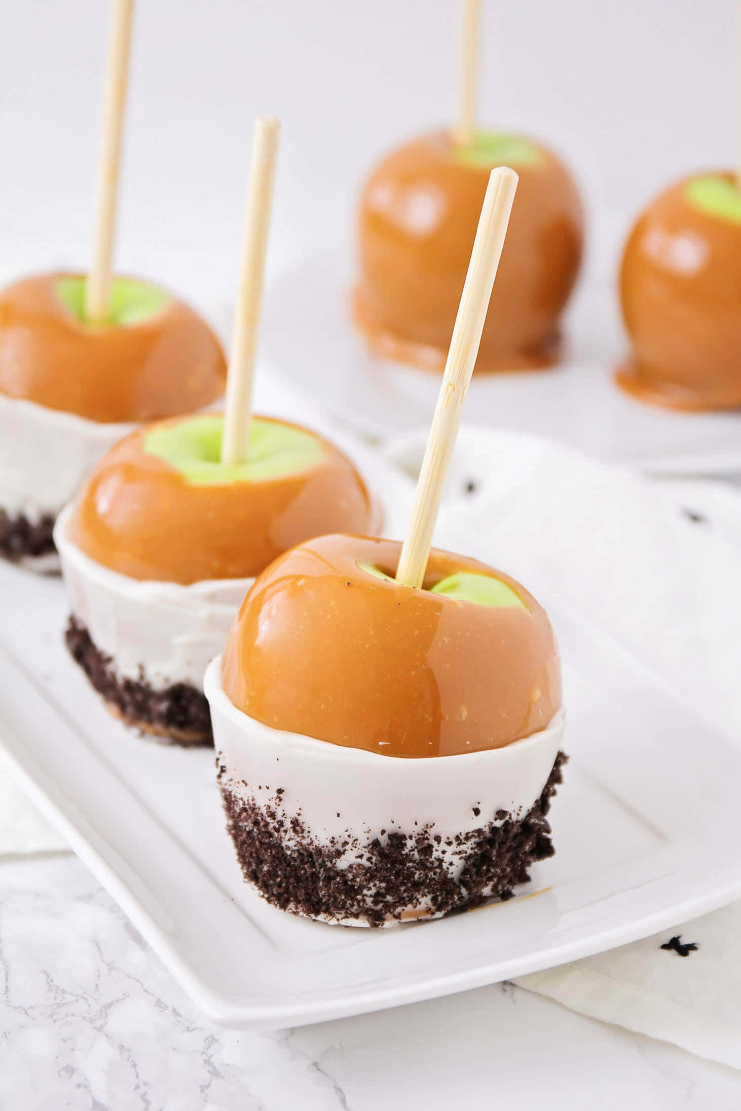 Caramel Apples 桌布 壁紙 — 閃亮焦糖蘋果置於白色奶油和巧克力碎餅底上，放在白色盤子中。