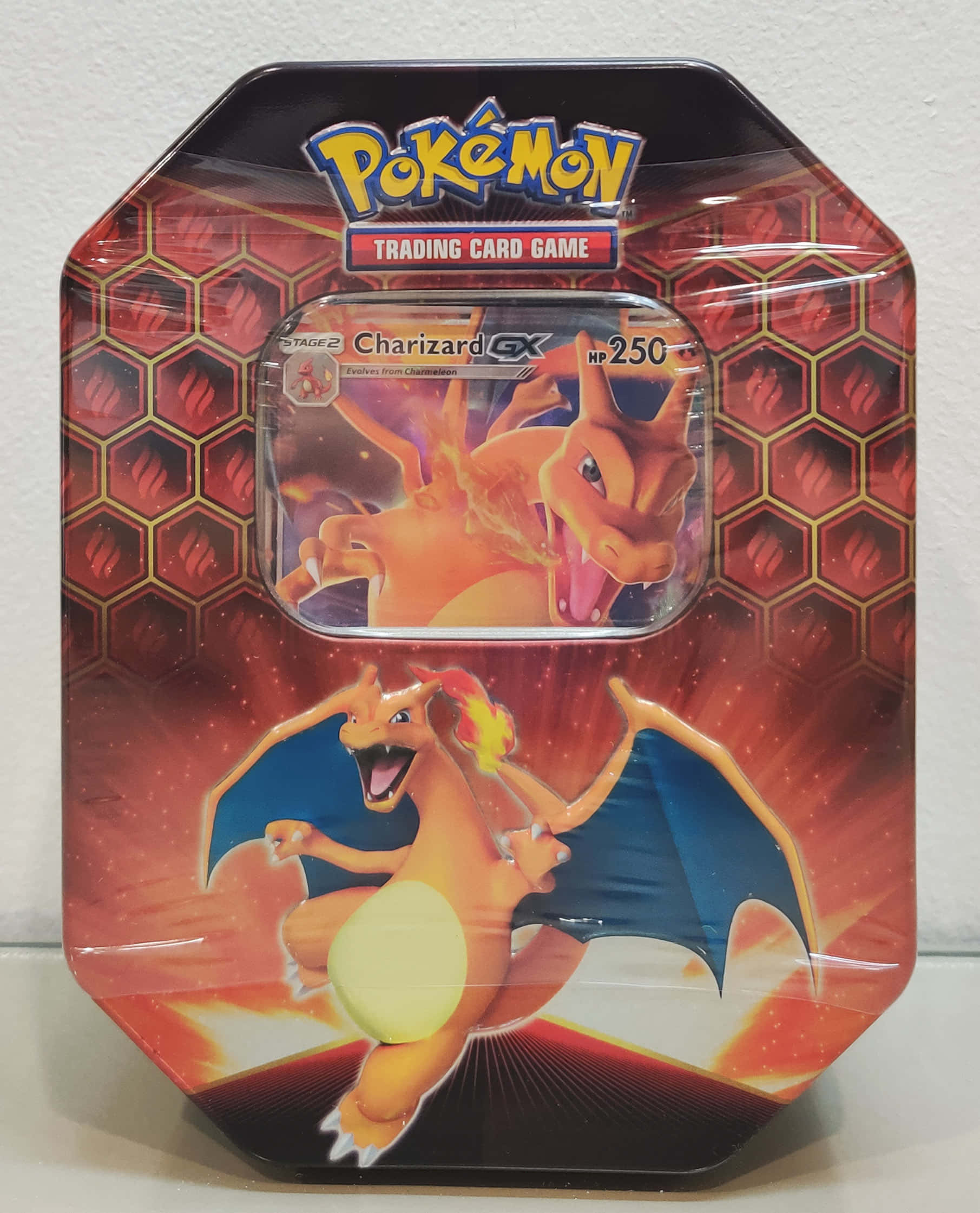 Charizard Pokemon 桌布 壁紙 — 閃亮的寶可夢集換式卡牌遊戲鐵盒， featuring Charizard GX，以火熱的橙色龍插圖搭配紅色六邊形背景。