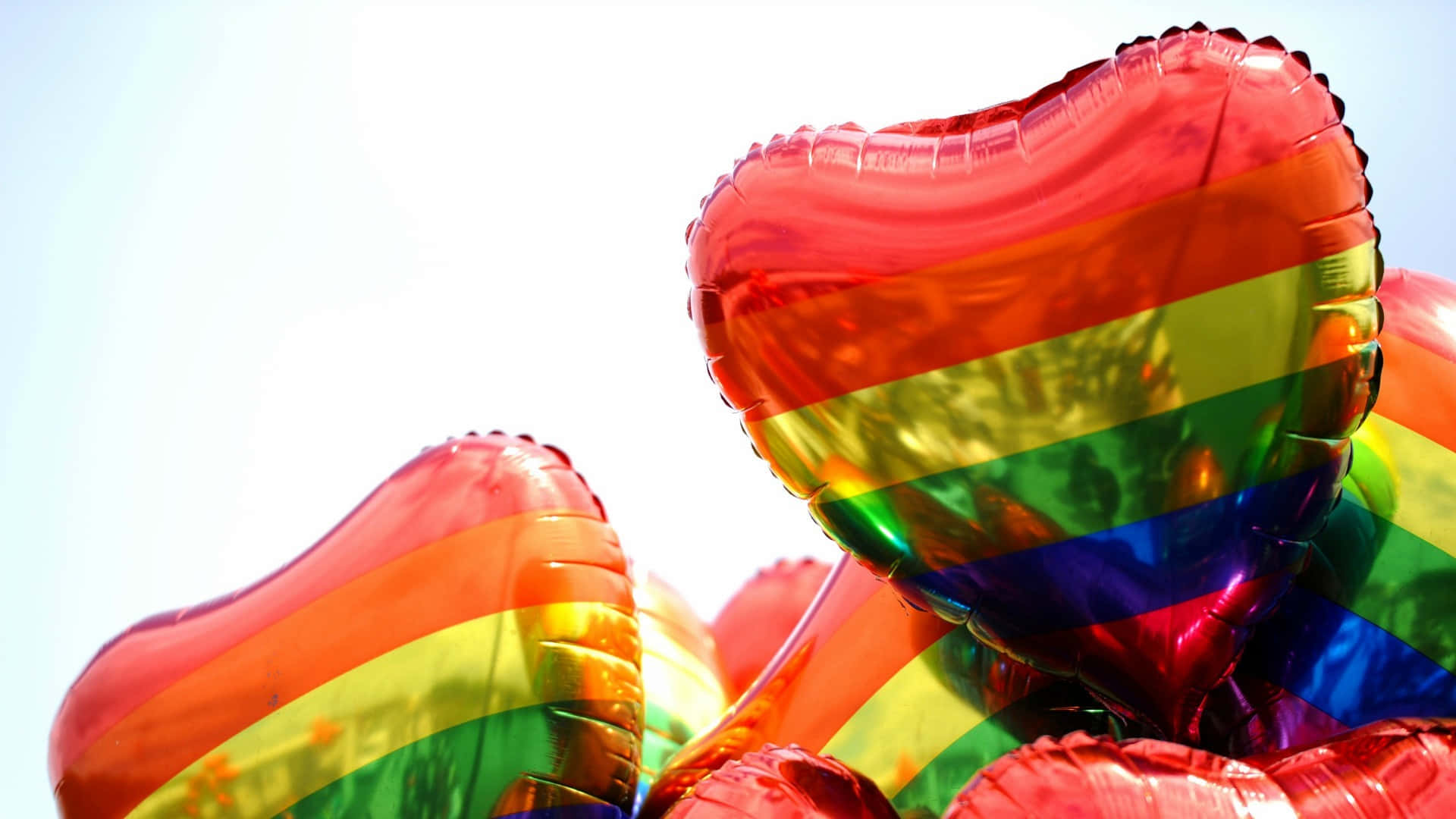 Pride Desktop 桌布 壁紙 — 閃亮的心形氣球帶有彩虹條紋，在明亮的天空中飄浮。