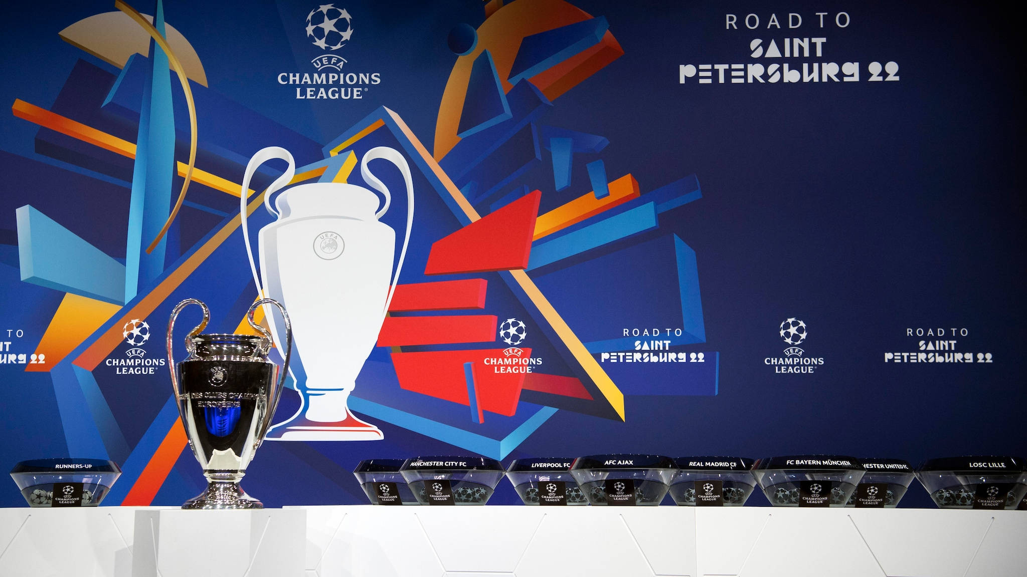 Uefa 桌布 壁紙 — 閃亮的歐冠獎盃展示在白色底座上，背景為鮮豔的藍色幾何圖案，並附有球隊名稱。