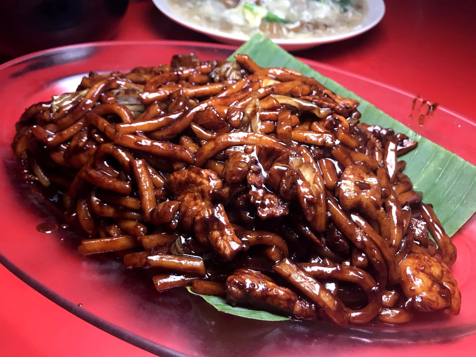 Noodles 桌布 壁紙 — 閃亮的炒麵搭配雞肉，濃郁深色醬汁，盛在紅色盤子上並附香蕉葉。