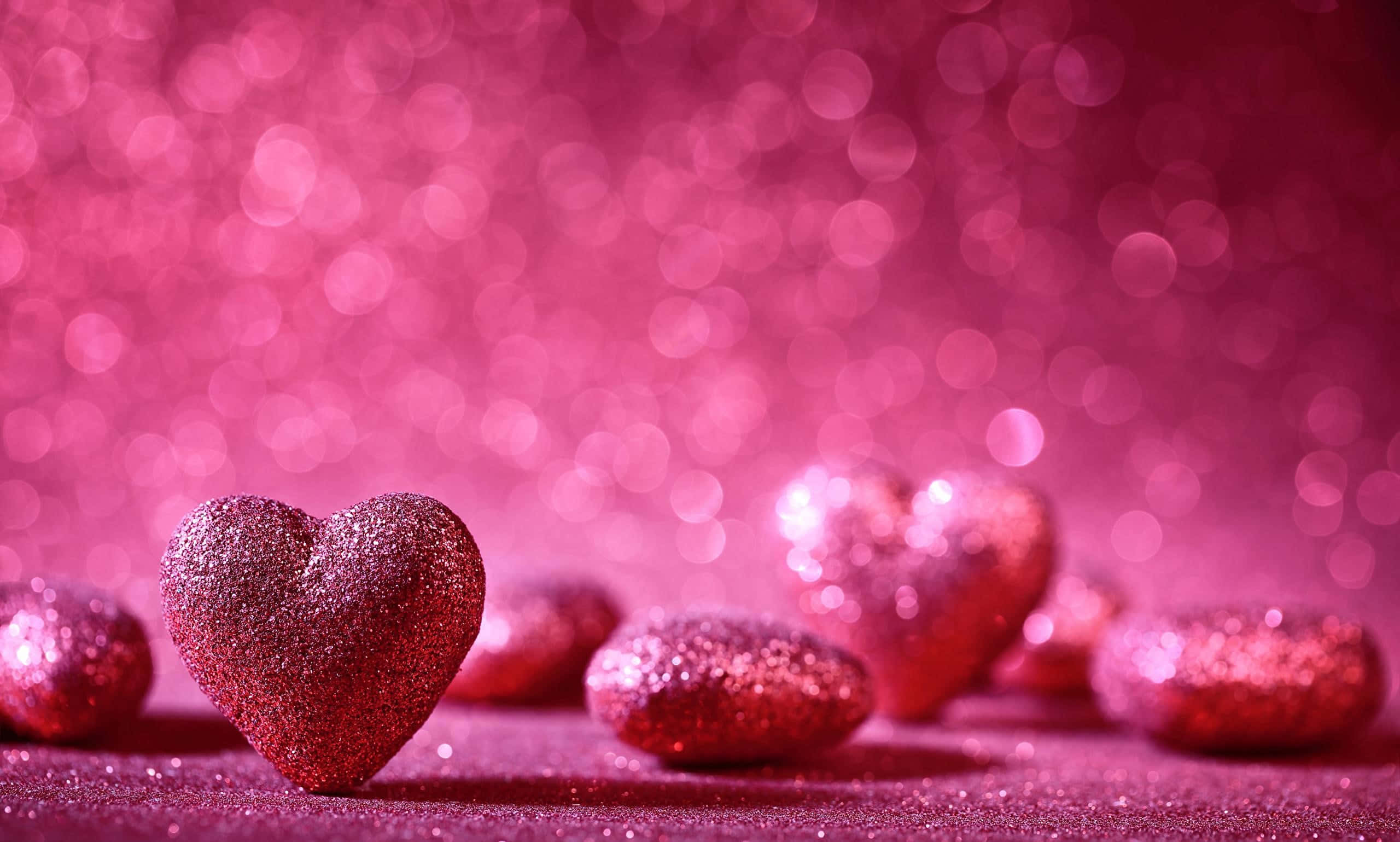 Glitter Pink Hearts 桌布 壁紙 — 閃亮的粉紅色閃粉心形散落在閃爍的表面上，背景是夢幻的散景。