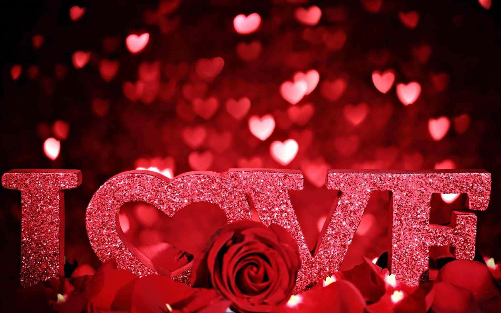 3d Love 桌布 壁紙 — 閃亮的紅色 'LOVE' 字母和一朵玫瑰放在花瓣上，背景是心形散景。