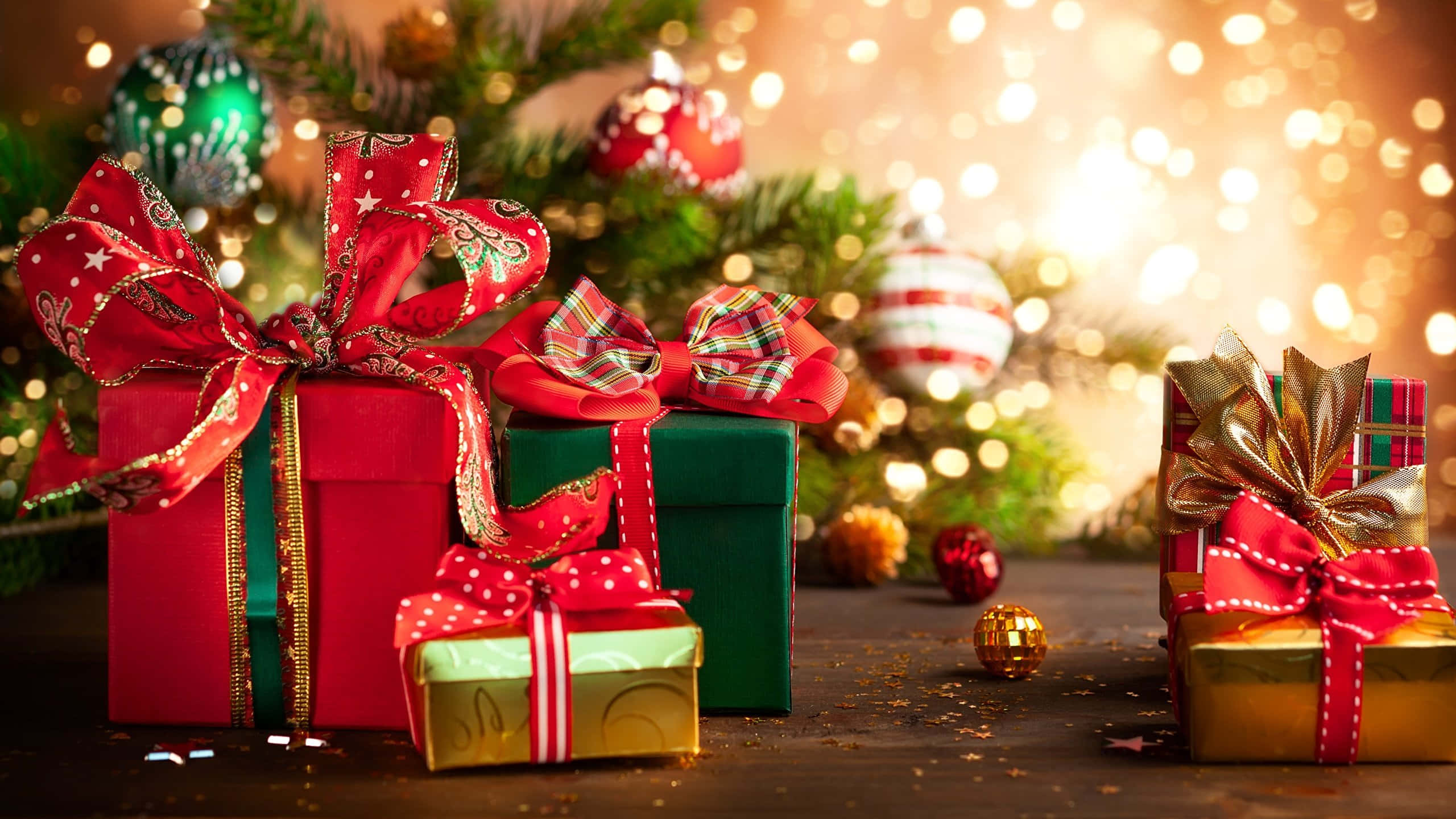 1920x1080 HD Christmas 桌布 壁紙 — 閃亮的紅色、綠色和金色禮物盒，飾以節日蝴蝶結，放在一個柔和模糊、散發溫暖散景燈光的聖誕樹前。