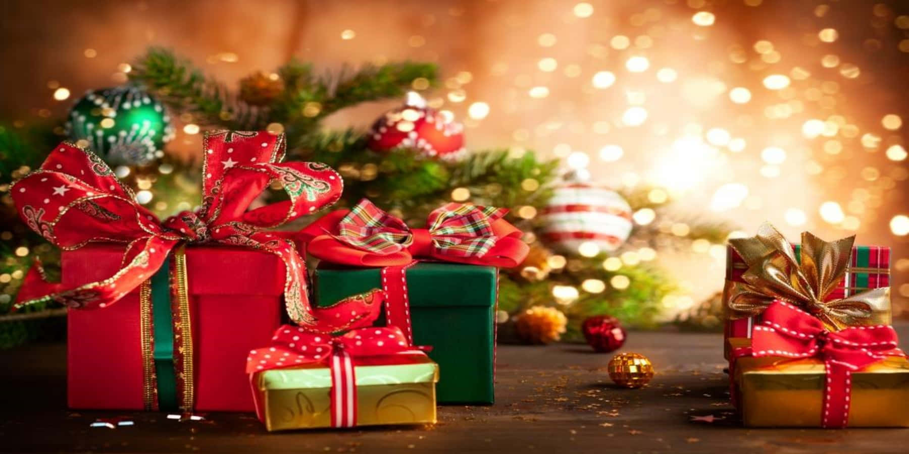 聖誕樹動畫 桌布 壁紙 — 閃亮的紅色、綠色和金色禮物盒飾以節日蝴蝶結，放在一個柔和模糊的聖誕樹前，聖誕樹散發著溫暖的散景燈光。