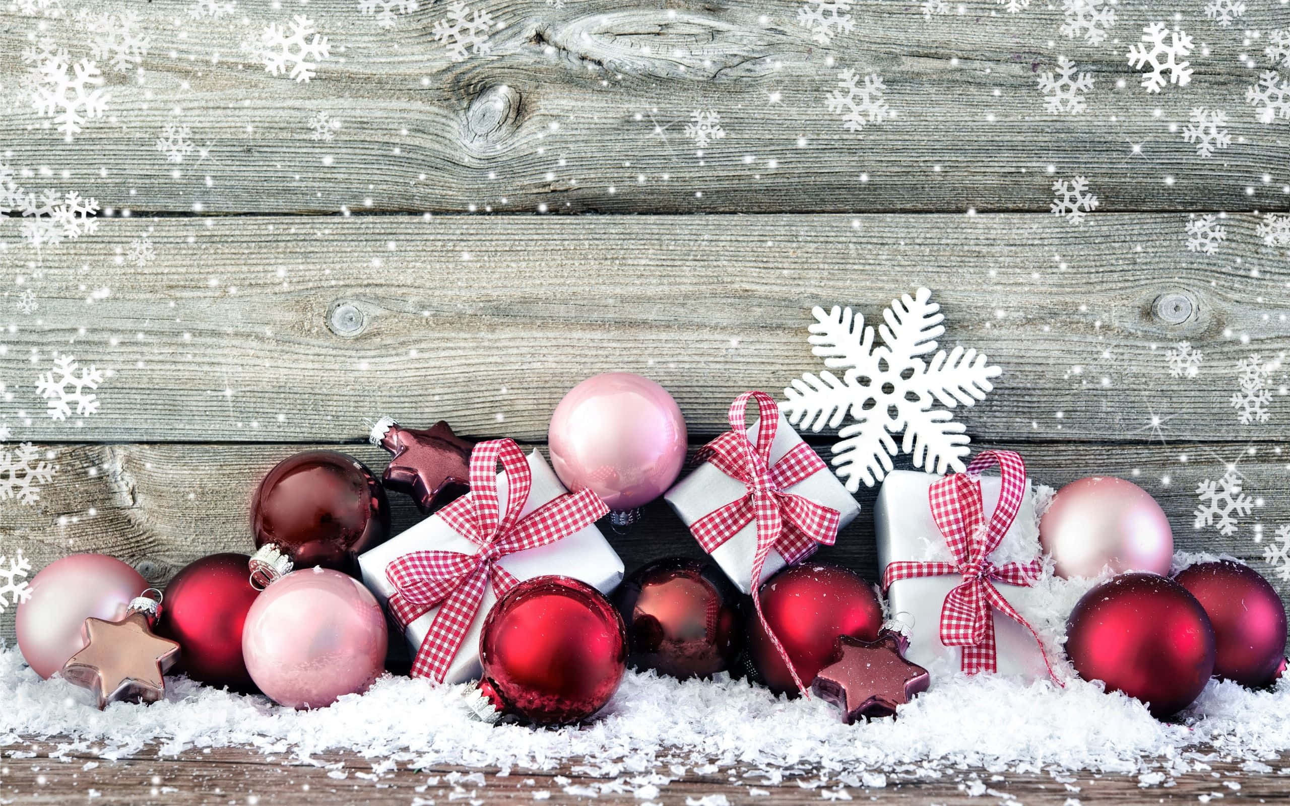 Christmas Ornament 桌布 壁紙 — 閃亮的紅色和粉紅色聖誕裝飾品和帶有紅色蝴蝶結的禮物盒放在雪白的木頭上，雪花飄落。