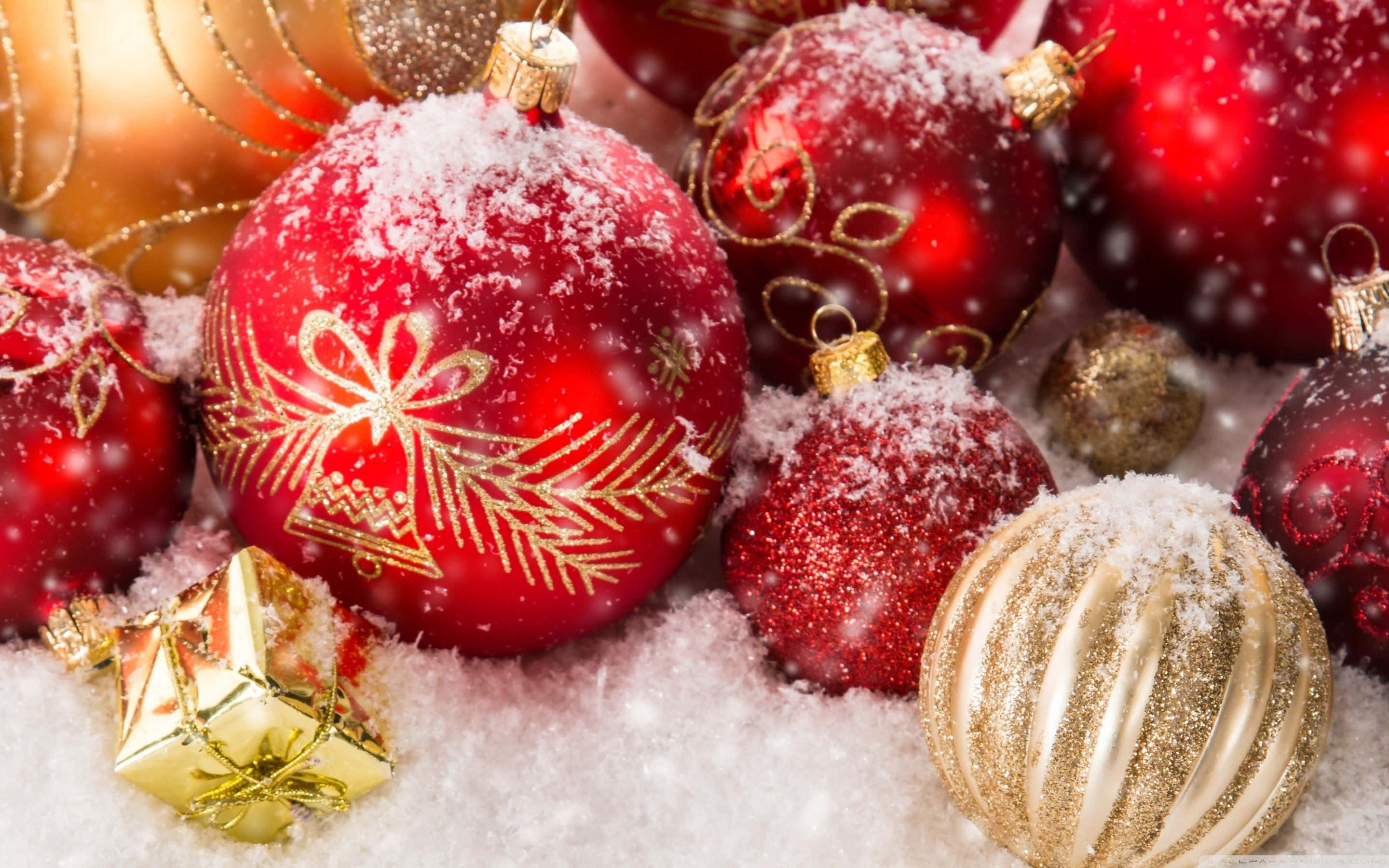 Christmas Balls 桌布 壁紙 — 閃亮的紅色和金色聖誕裝飾品上撒滿雪花，放在雪地上，雪花飄落。