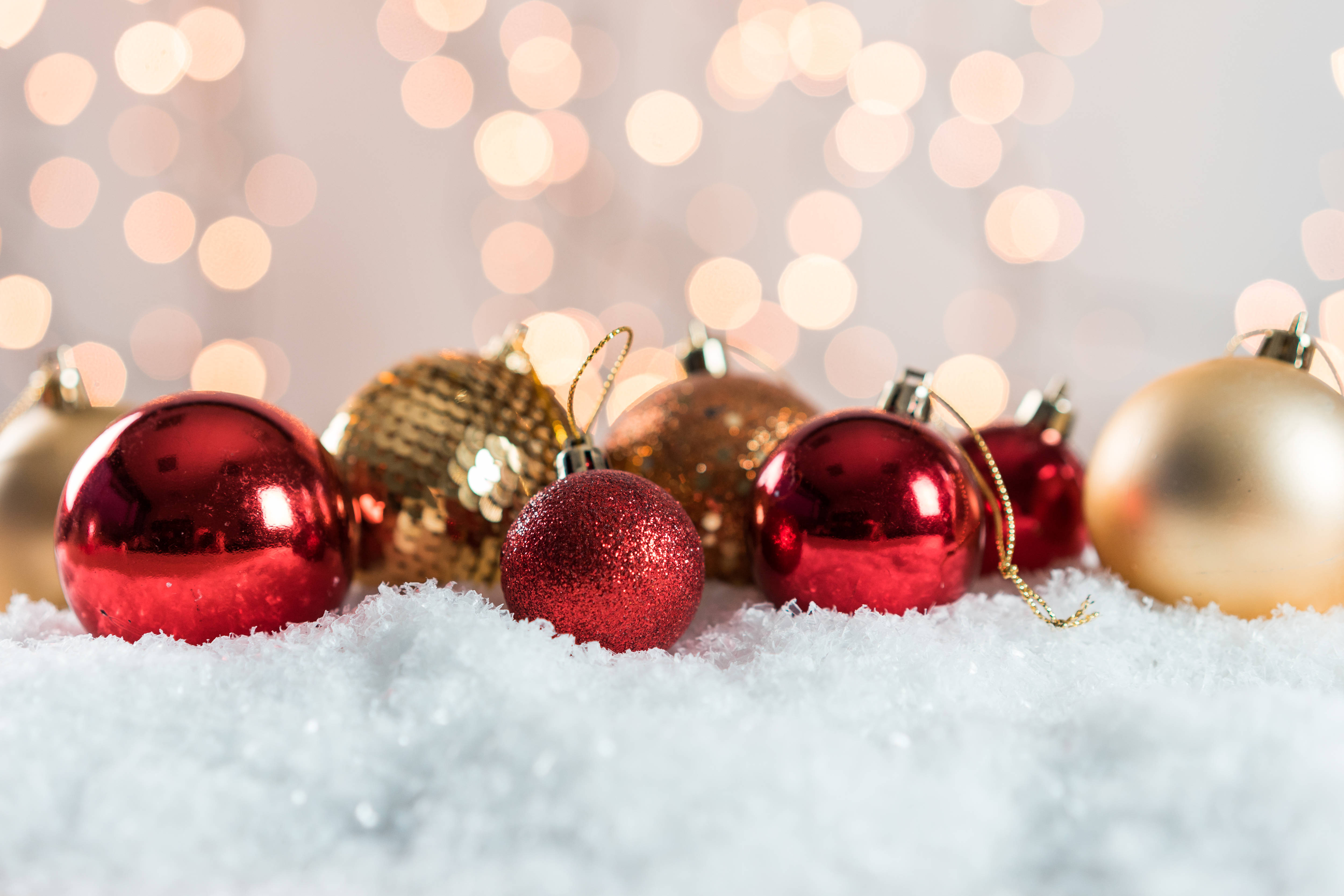 Red Christmas 桌布 壁紙 — 閃亮的紅色和金色聖誕裝飾品放在蓬鬆的白雪中，溫暖的散景燈光在後面柔和地發光。