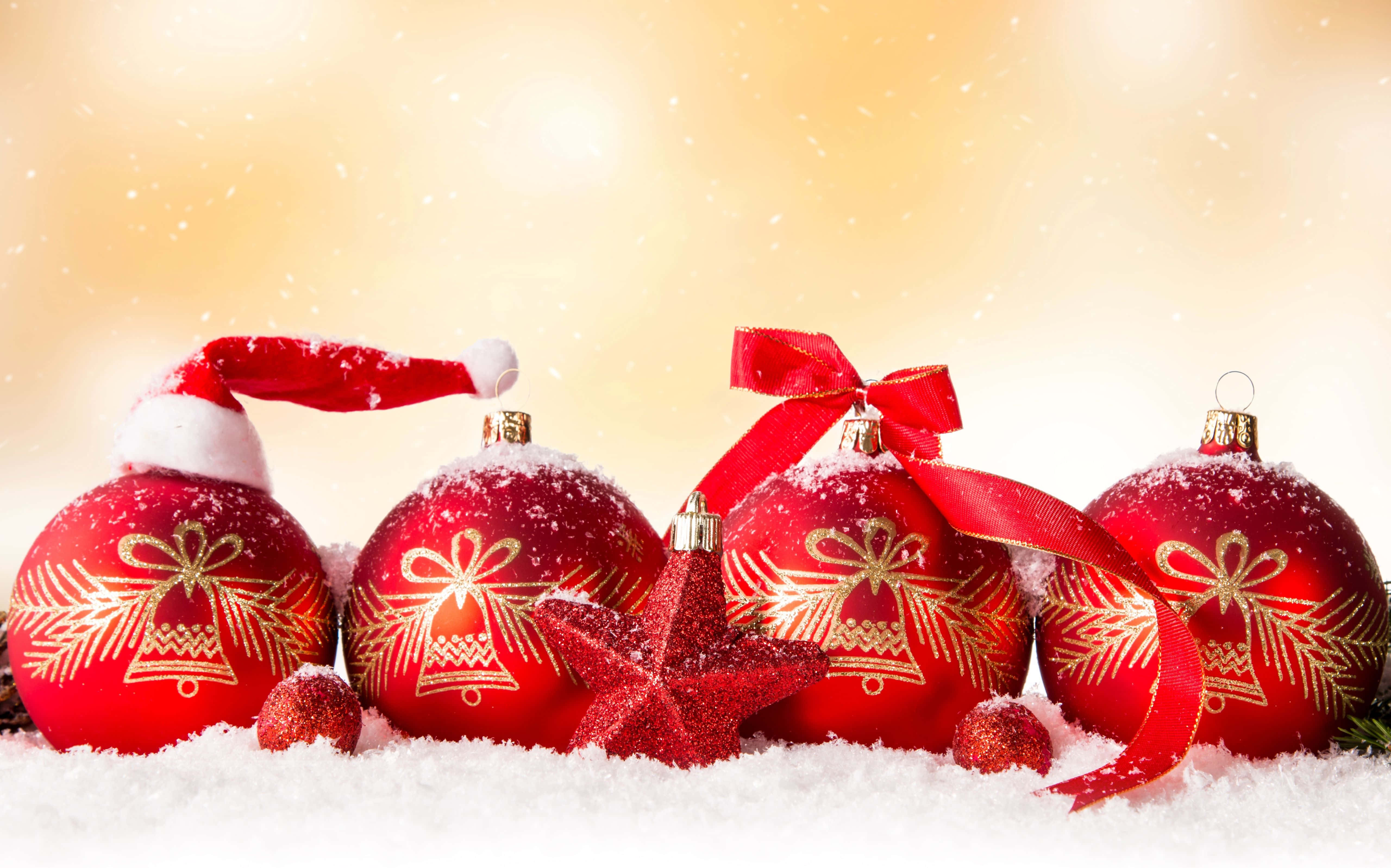 Christmas Ornament 桌布 壁紙 — 閃亮的紅色聖誕裝飾品，配有金色鈴鐺和雪塵，躺在柔軟的白雪上，背景是溫暖的金色。