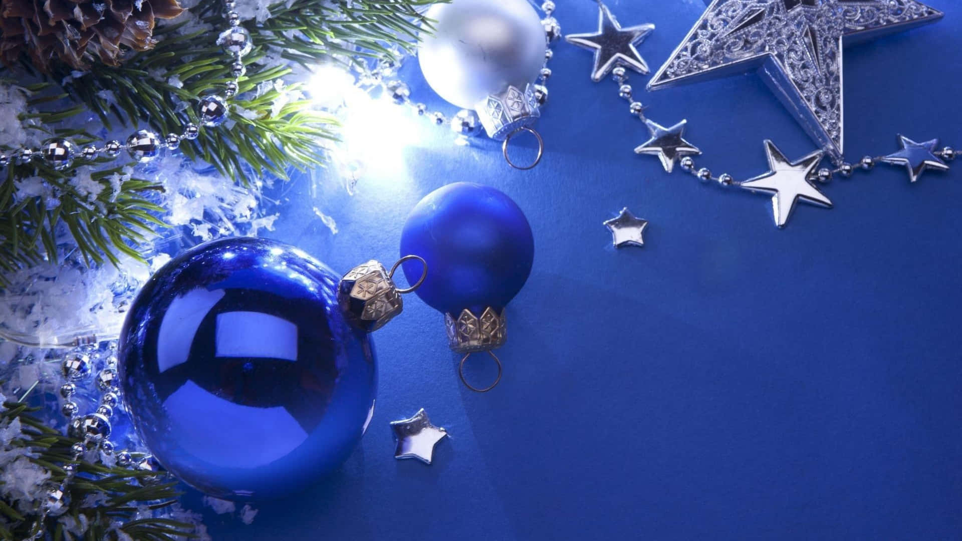 Christmas Star 桌布 壁紙 — 閃亮的藍色裝飾品、銀色星星和松針在明亮的燈光下，在深藍色的節日表面上閃耀。