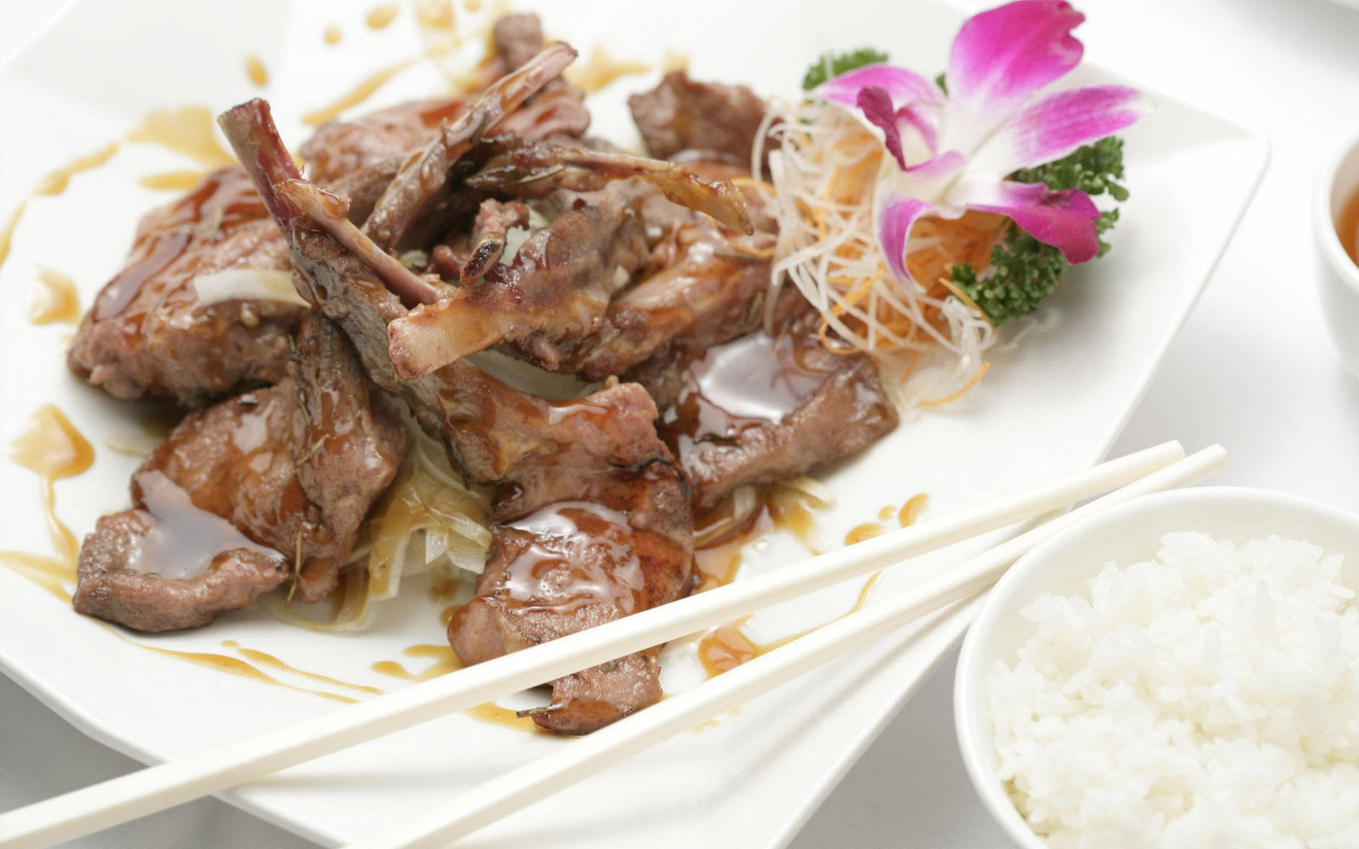 4K Food 桌布 壁紙 — 閃亮的釉面肉塊，配上洋蔥裝飾和粉紅色蘭花，放在白色盤子上，旁邊有飯和筷子。