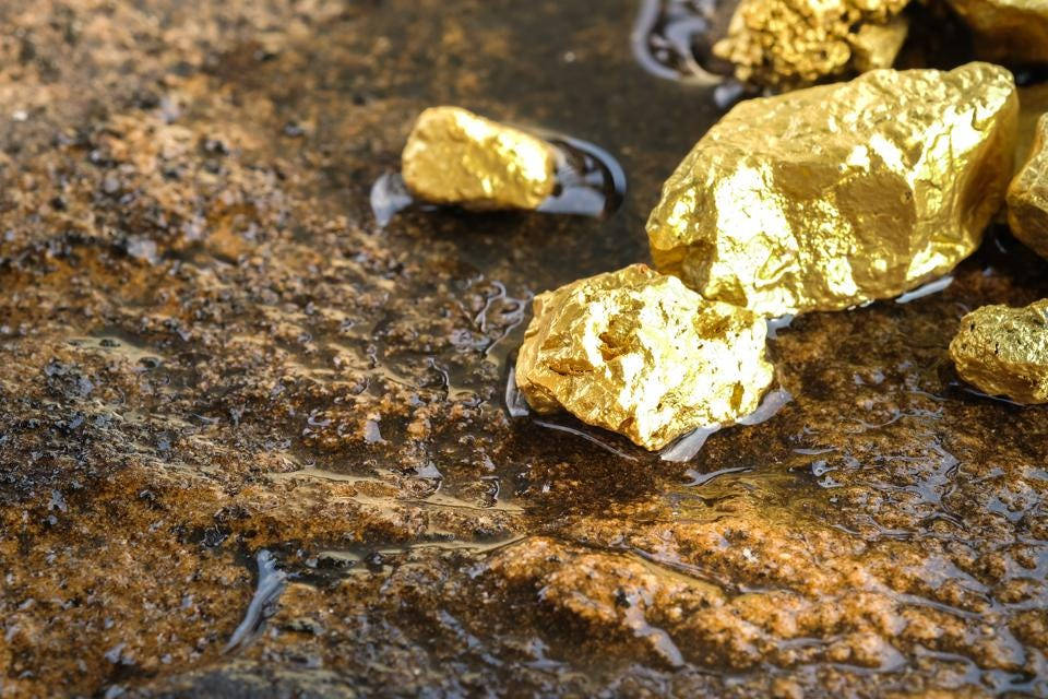 Rock 桌布 壁紙 — 閃亮的金塊躺在淺水中，位於潮濕、有紋理的岩石表面上，反射光線。