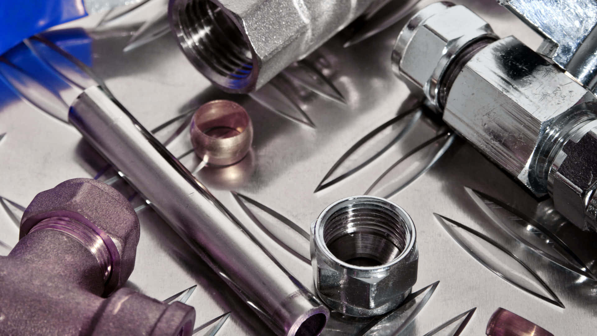 Plumbing 桌布 壁紙 — 閃亮的金屬水管零件和工具散落在鑽石紋板面上，帶有銳利反光。