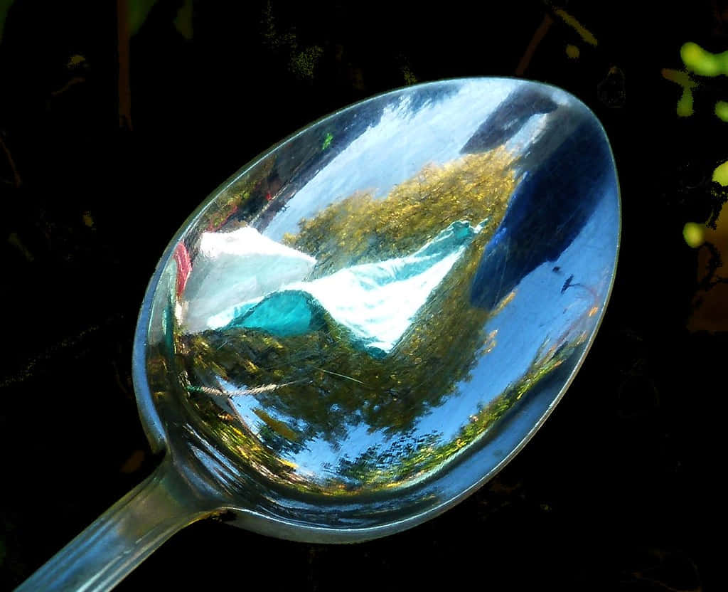 reflection 桌布 壁紙 — 閃亮的金屬湯匙在深色背景上反射出充滿活力的山湖景色，並帶有綠色樹葉。