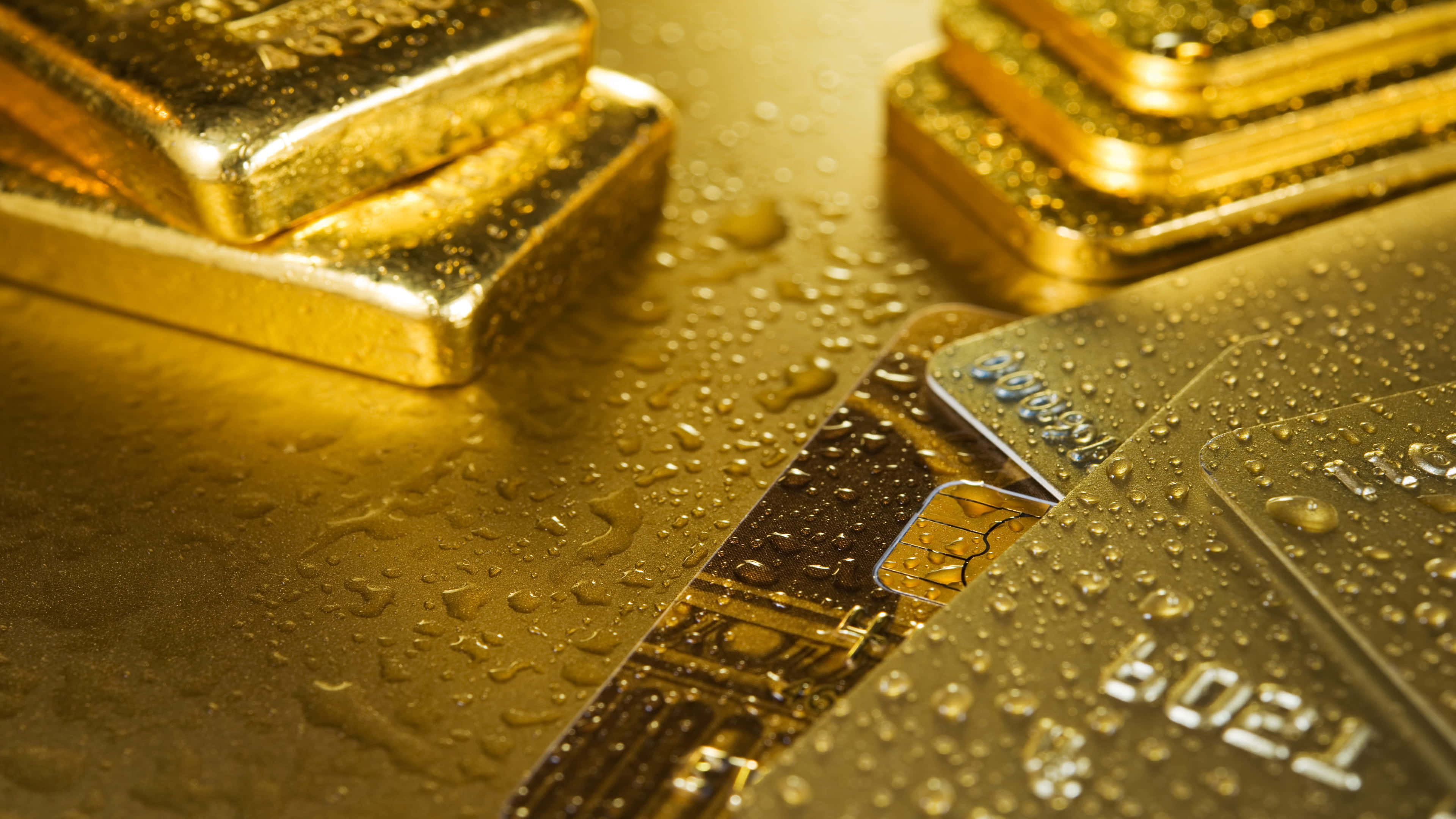 Shiny Gold 桌布 壁紙 — 閃亮的金條和信用卡在反光的金色表面上閃爍著水滴。