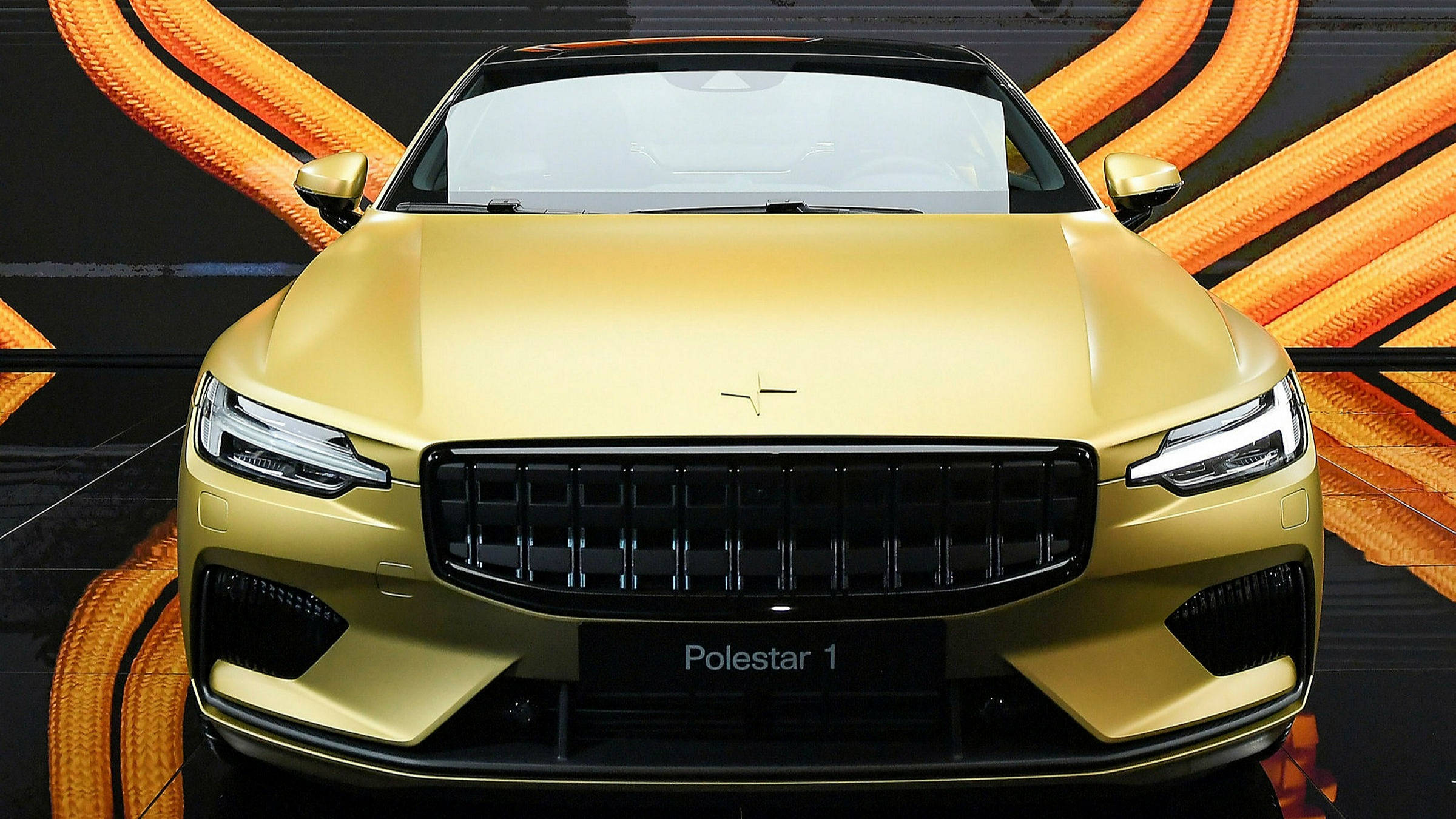 豪華車 桌布 壁紙 — 閃亮的金色Polestar 1跑車在工作室環境中，以動態的橙色電纜背景展示。
