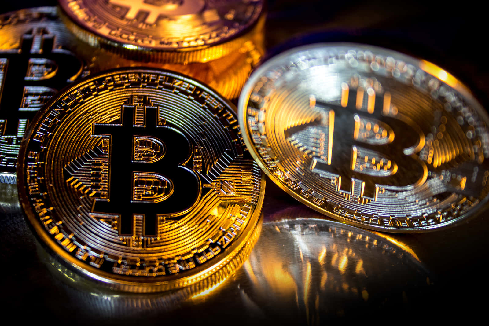 比特幣 桌布 壁紙 — 閃亮的金色和銀色比特幣硬幣在黑暗表面上反射溫暖光線，景深較淺。