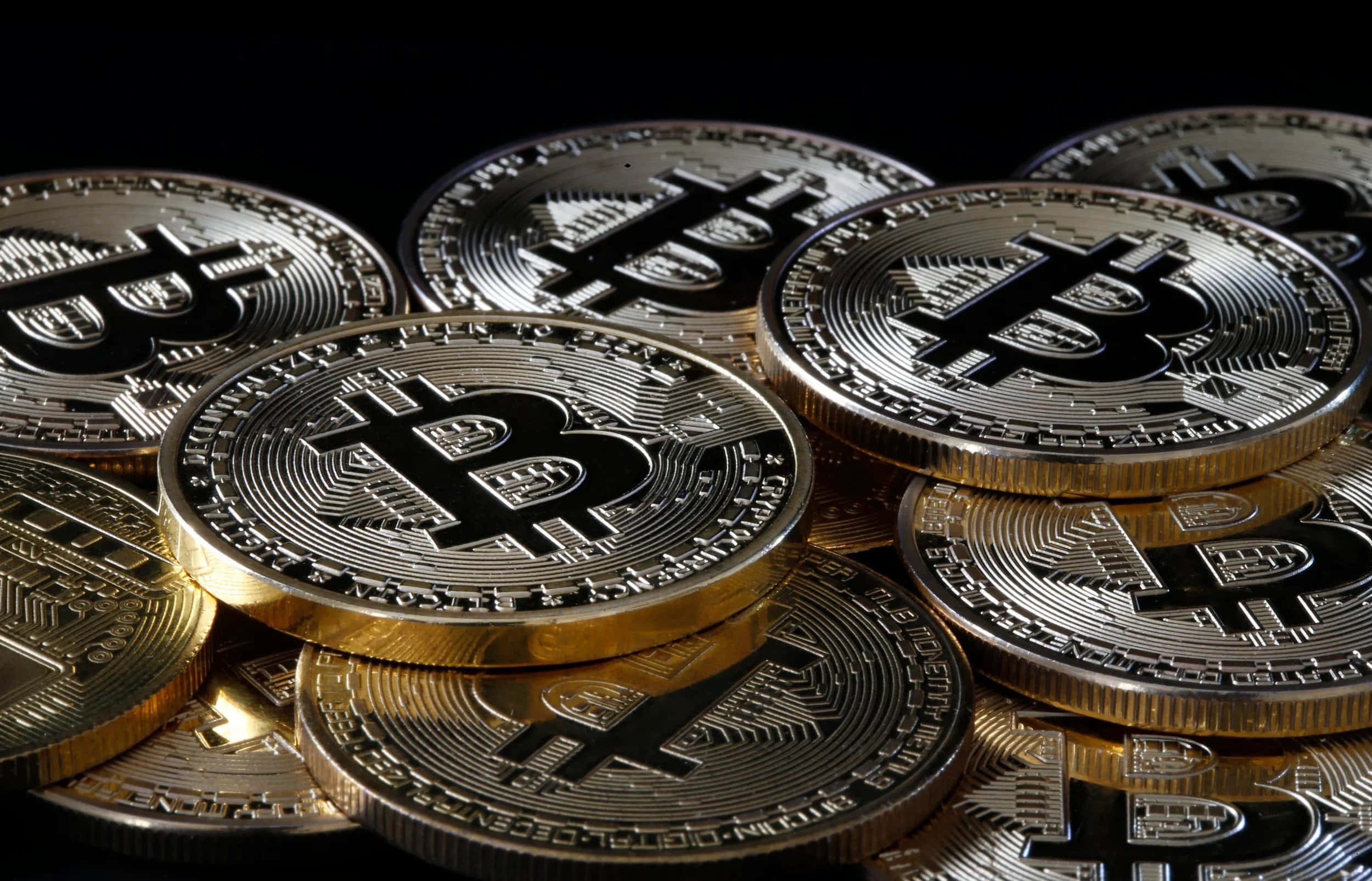 比特幣 桌布 壁紙 — 閃亮的金色比特幣堆疊在黑色背景上，帶有反射高光。