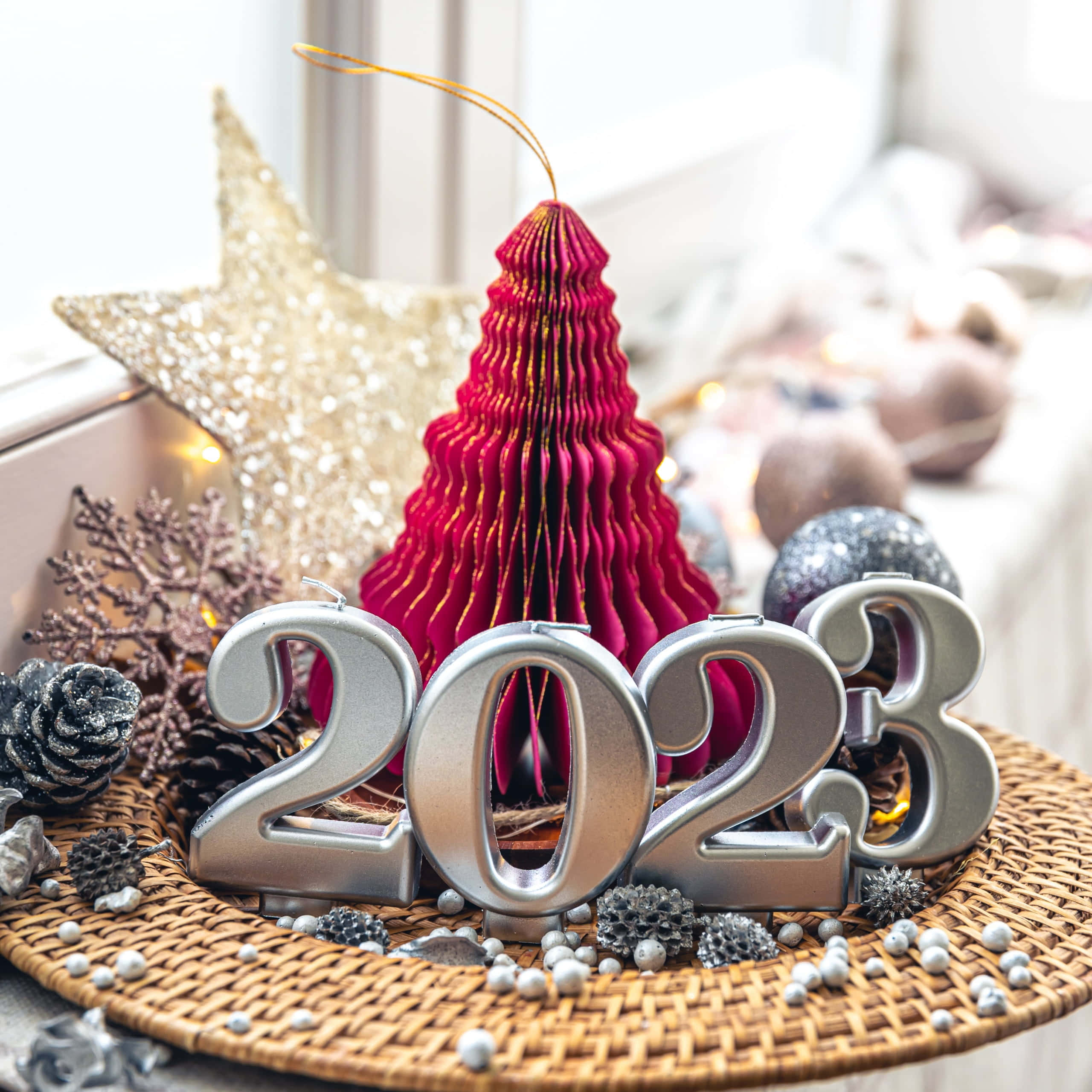 新年 桌布 壁紙 — 閃亮的銀色2023數字放在編織墊上，周圍環繞著節日紅色聖誕樹裝飾、松果和閃爍的星星裝飾。