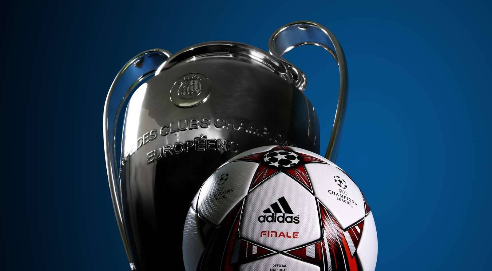 Champions League 桌布 壁紙 — 閃亮的銀色UEFA歐冠獎盃和官方比賽用球在深藍色漸變背景上。