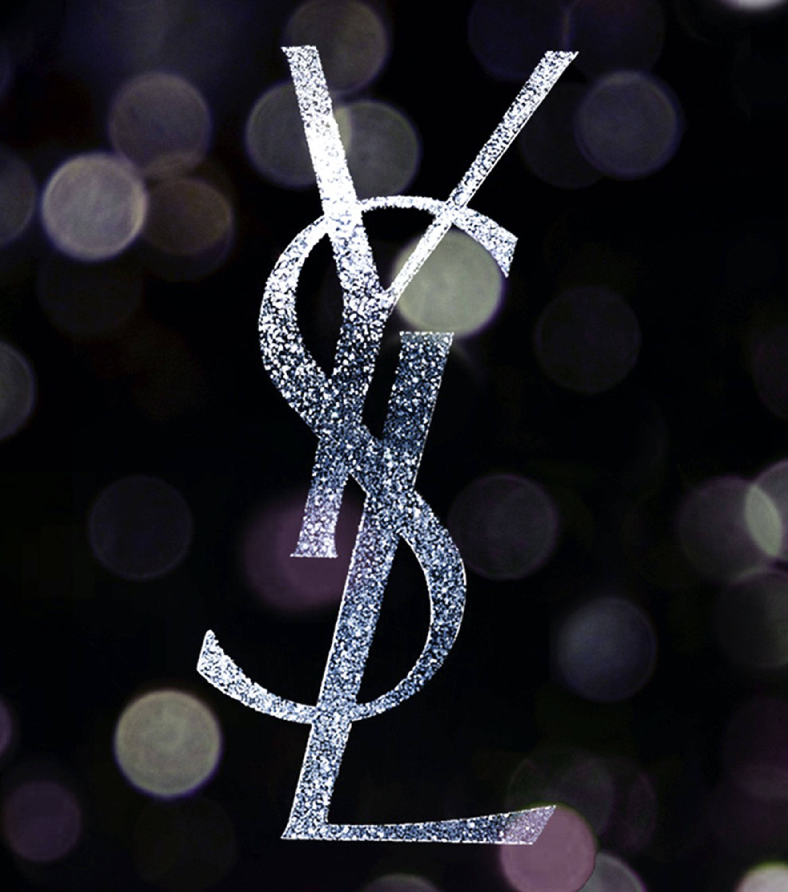 Ysl 桌布 壁紙 — 閃亮的銀色YSL標誌在帶有柔和紫色散景燈光的深色背景上脫穎而出。