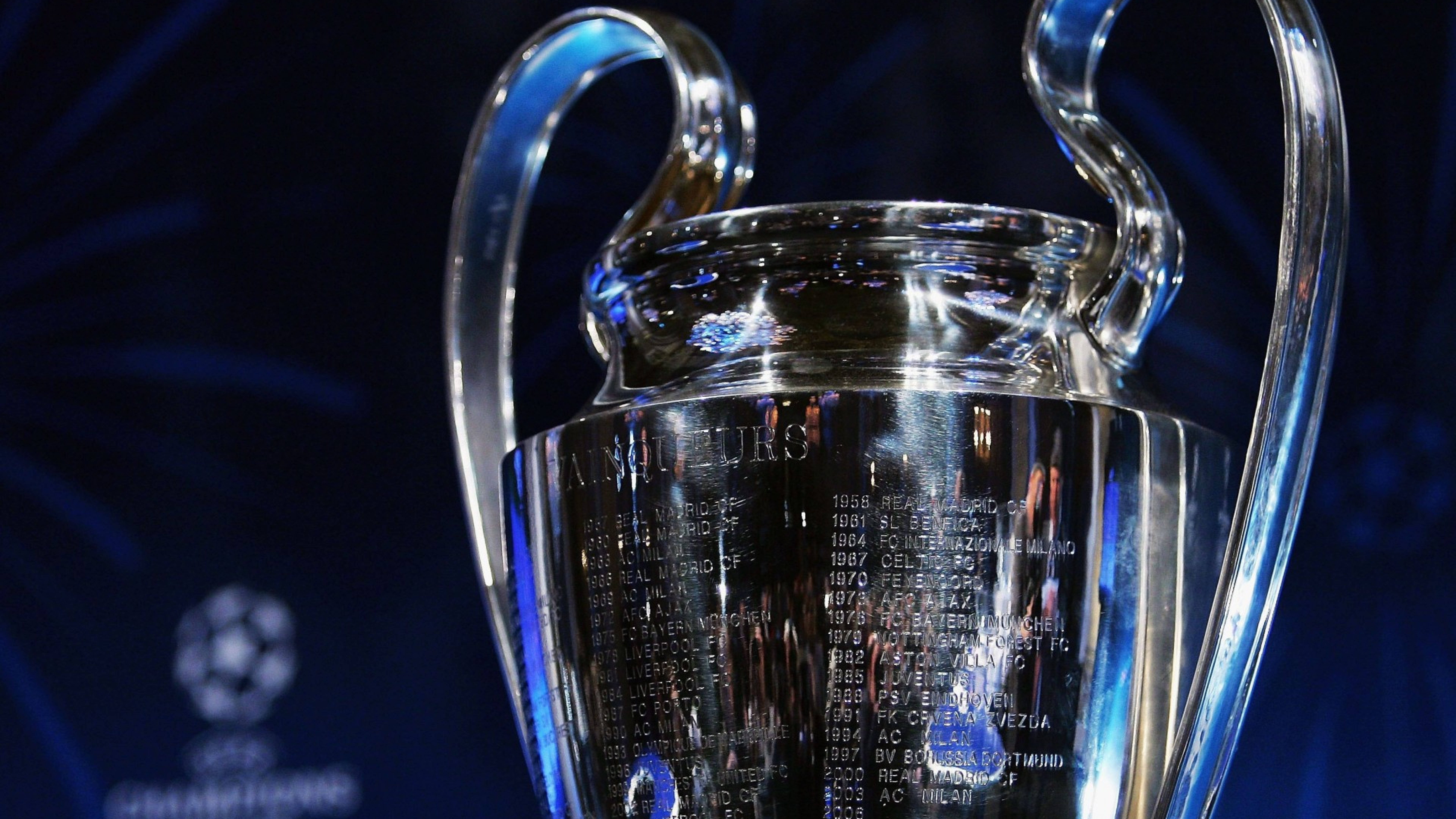 Champions League 桌布 壁紙 — 閃亮的銀色歐洲冠軍聯賽獎盃在深色背景下反射藍光，上面刻有冠軍名字。