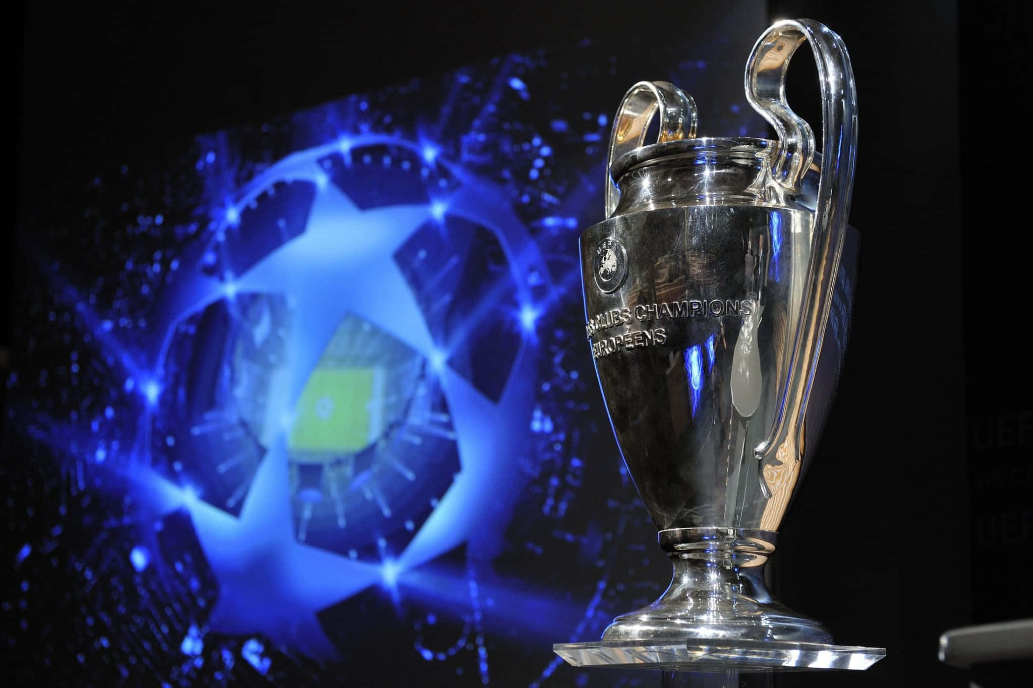 Champions League 桌布 壁紙 — 閃亮的銀色歐洲聯賽冠軍盃在聚光燈下，以發光的藍色球場投影背景閃爍。