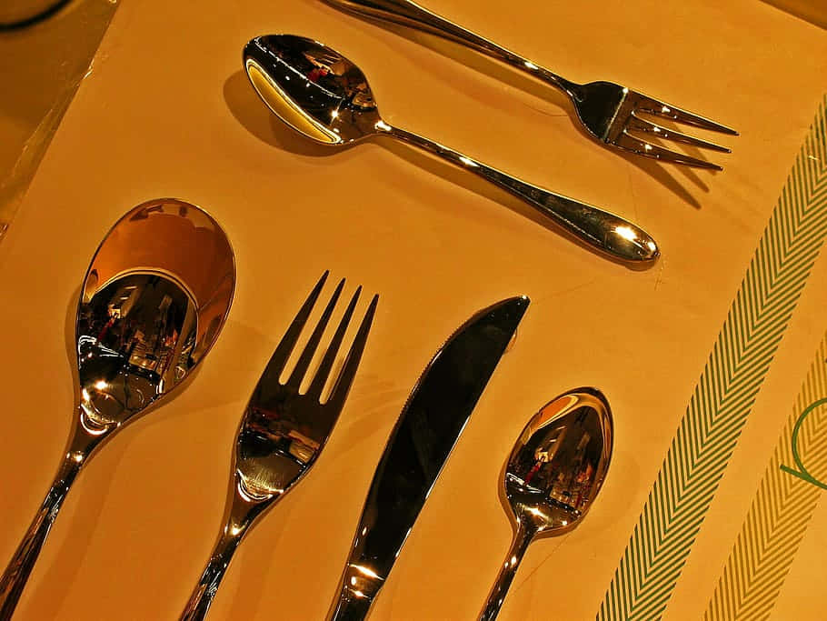 kitchen 桌布 壁紙 — 閃亮的銀色餐具擺放在暖色調的幾何綠色圖案桌布上，反射環境光線。