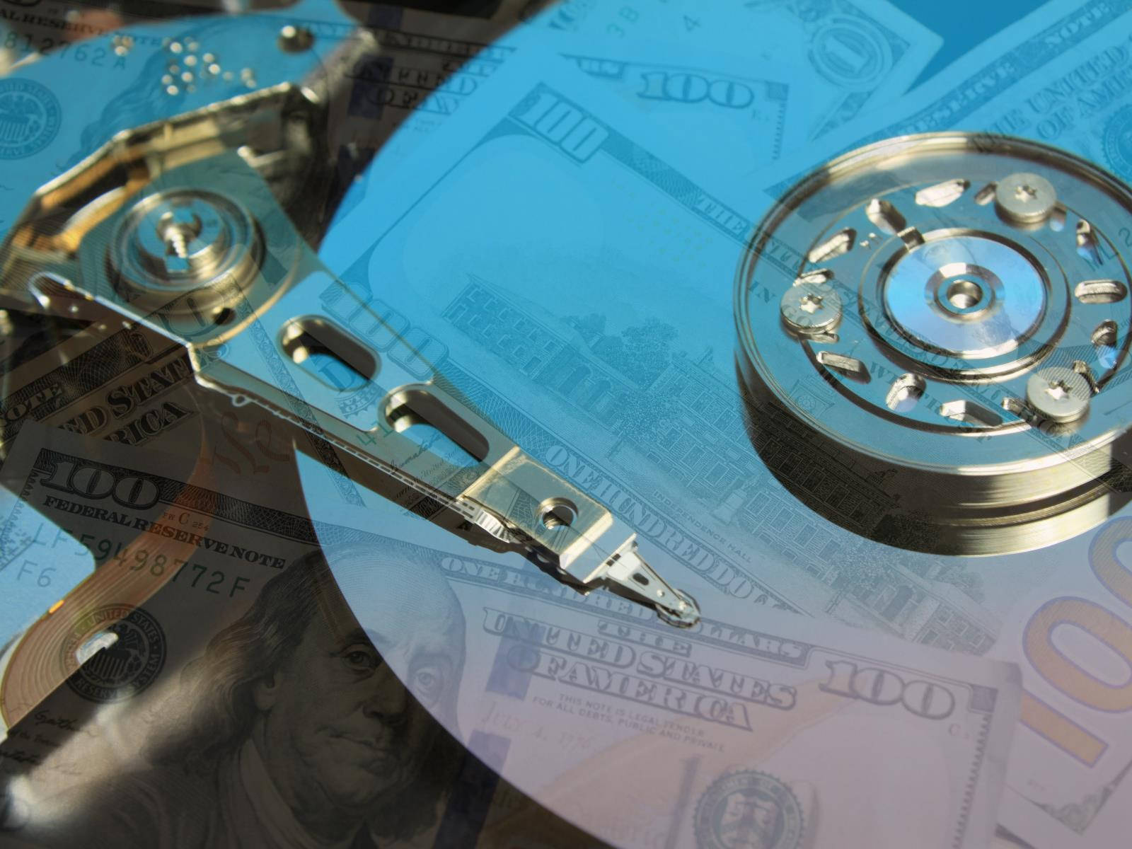 Hard Drive 桌布 壁紙 — 閃亮的開放式硬碟碟片放在帶有藍色調的百元美鈔上，象徵數位資料和金融價值。