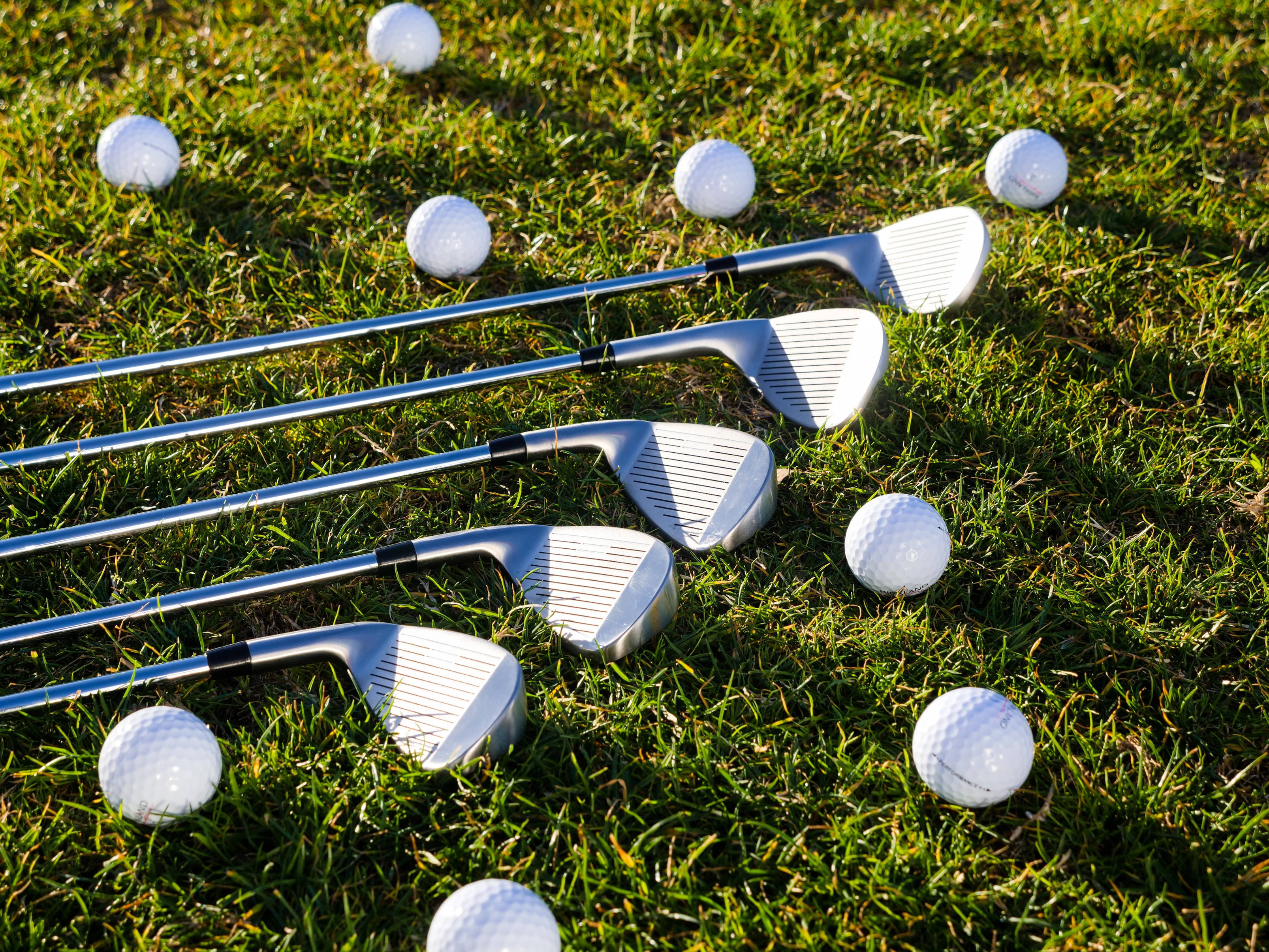 4K Golf 桌布 壁紙 — 閃亮的高爾夫球桿和白色高爾夫球在明亮的戶外環境中，躺在陽光照耀的綠色草地上。