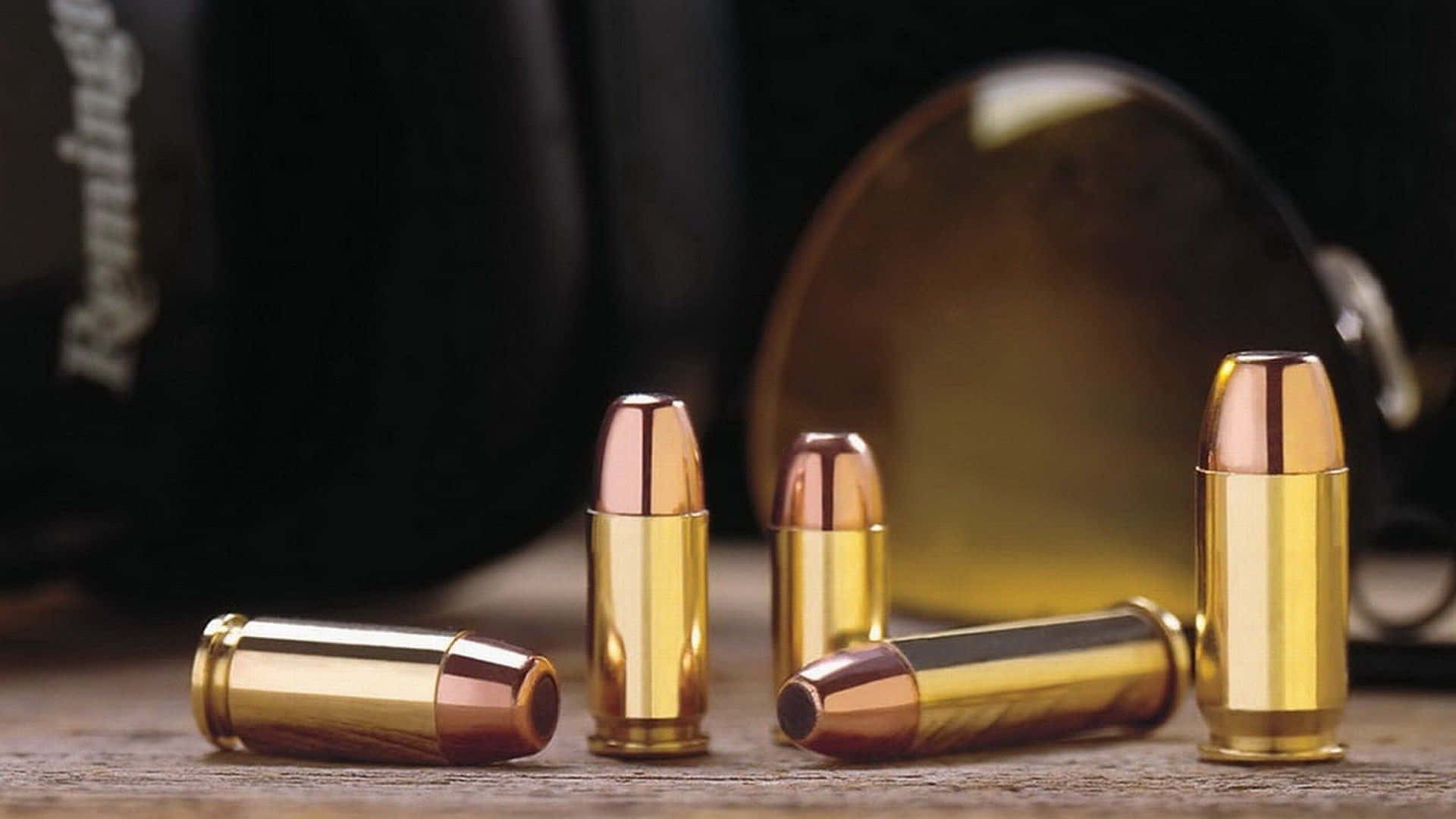 bullet 桌布 壁紙 — 閃亮的黃銅和銅製子彈排列在木質表面上，背景有模糊的槍械。
