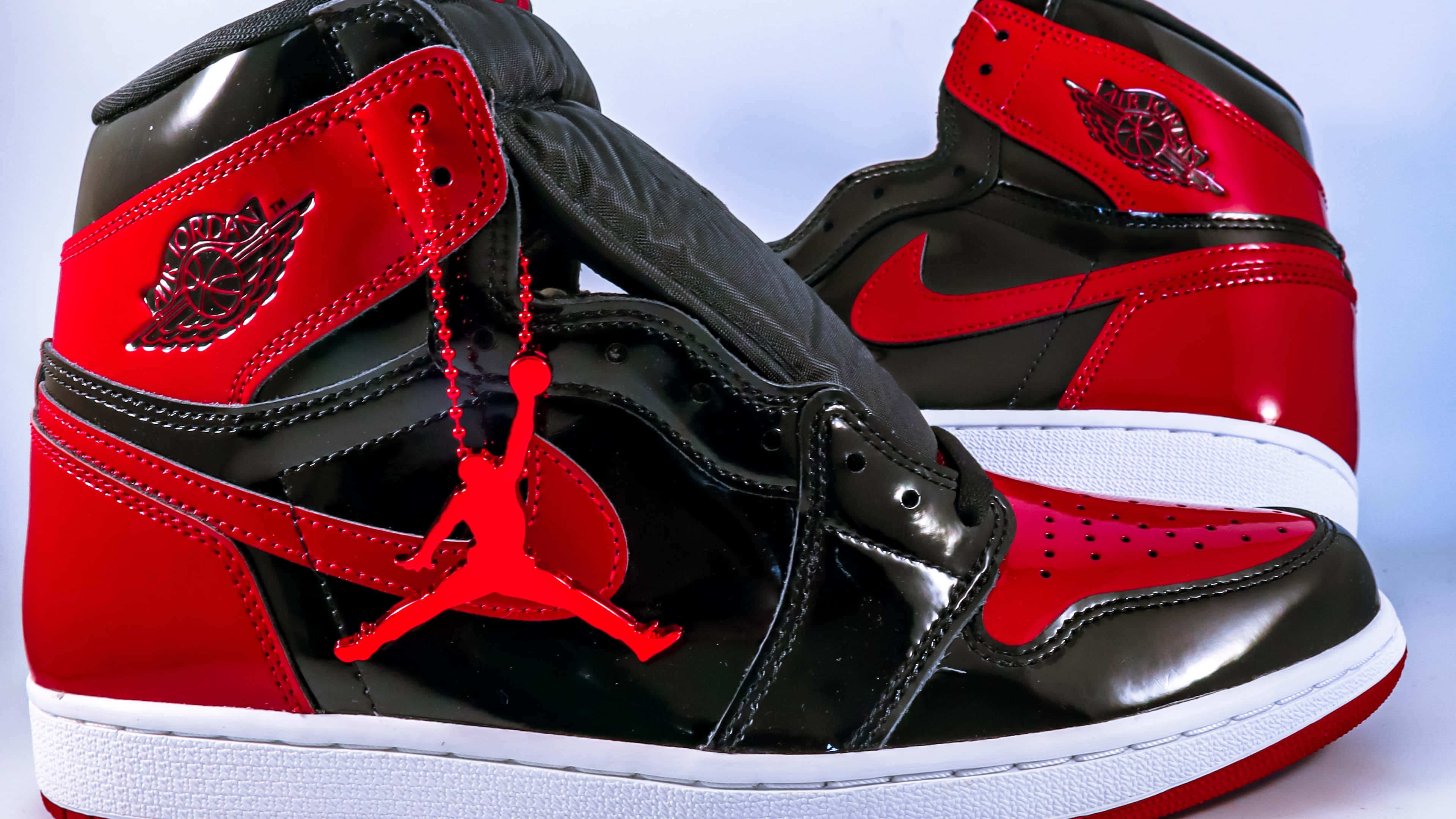 4K 桌布 壁紙 — 閃亮的黑色和紅色 Jordan 1 運動鞋，鞋帶上掛著標誌性的 Jumpman 標誌，背景為柔和的藍色。