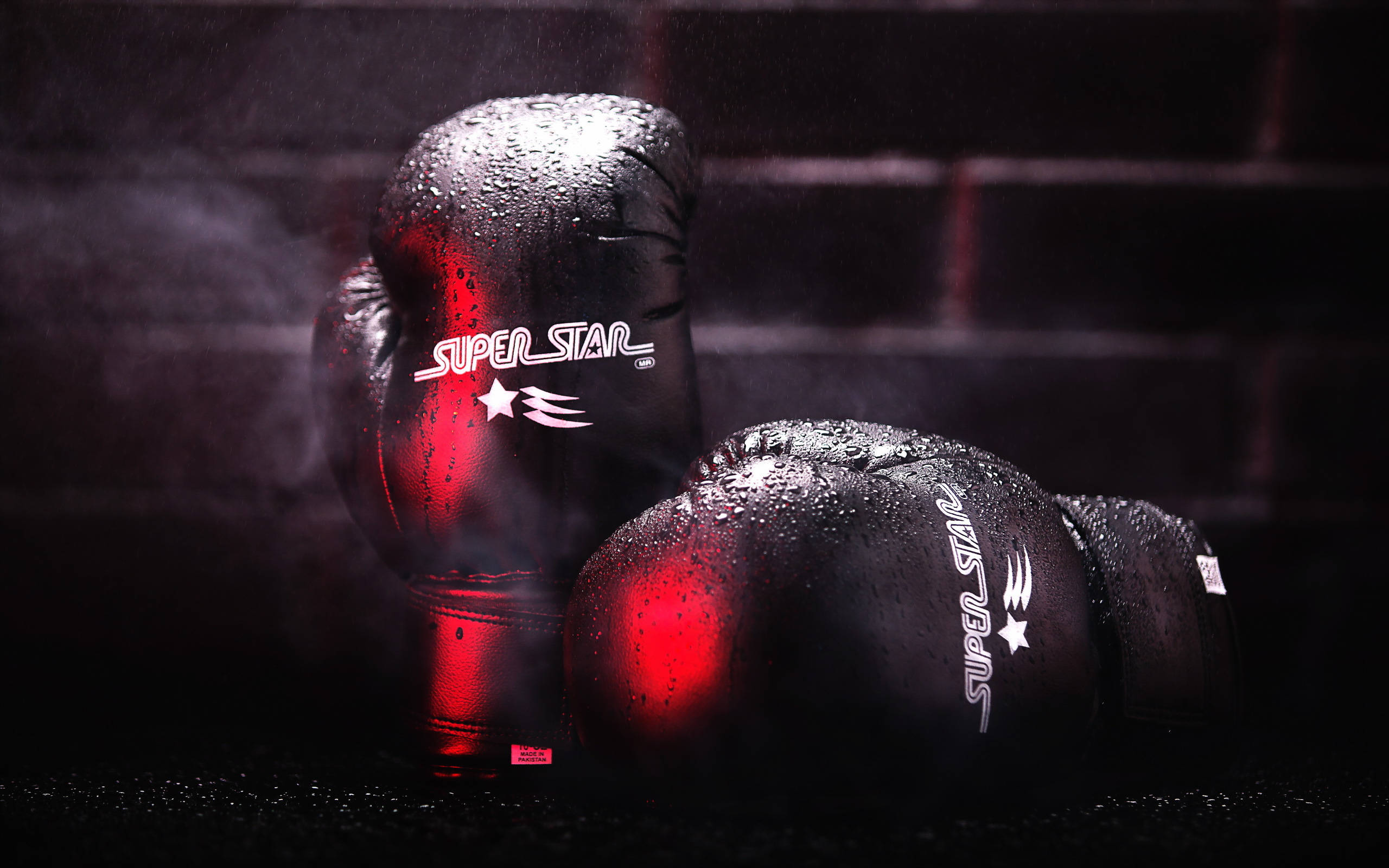 Boxing 桌布 壁紙 — 閃亮的黑色拳擊手套帶有紅色燈光，放在深色表面上，背景是磚牆，霧氣在周圍旋轉。