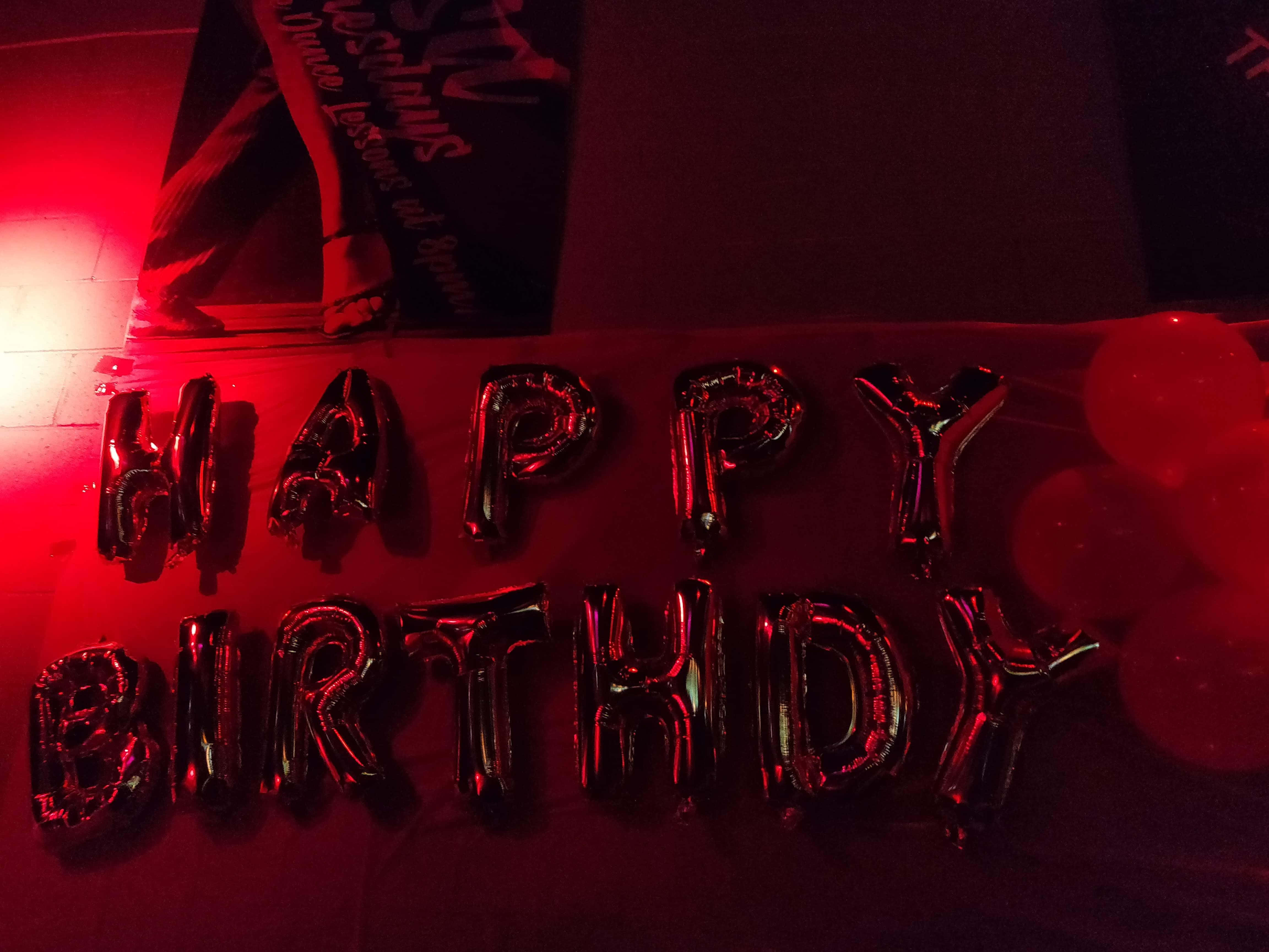 生日快樂 桌布 壁紙 — 閃亮的黑色箔氣球在戲劇性的紅光下拼出 HAPPY BIRTHDAY，附近有圓形氣球。