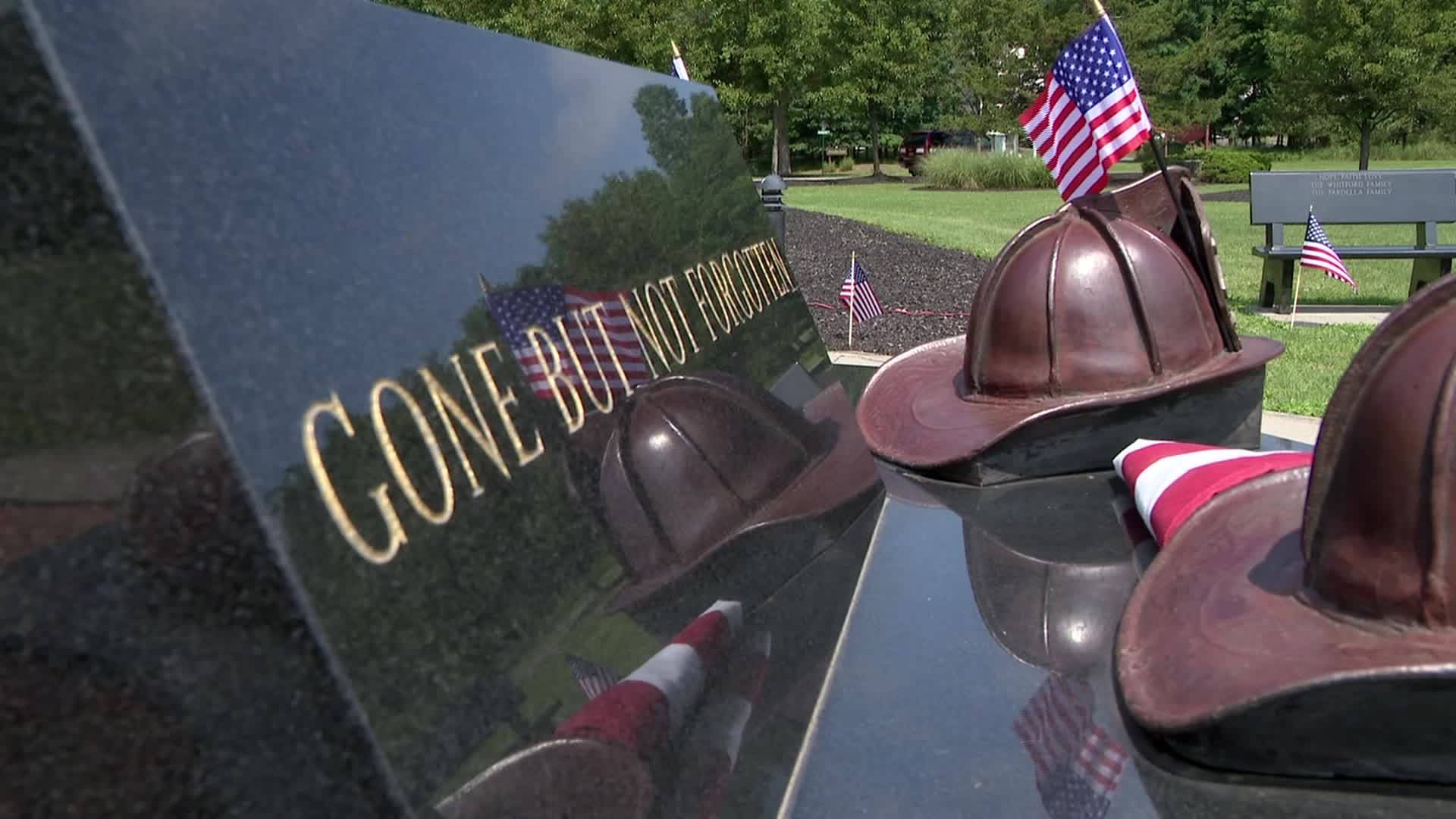 911 Memorial 桌布 壁紙 — 閃亮的黑色紀念牌匾，金色字體寫著「gone but not forgotten」，周圍環繞著消防員頭盔和美國國旗。