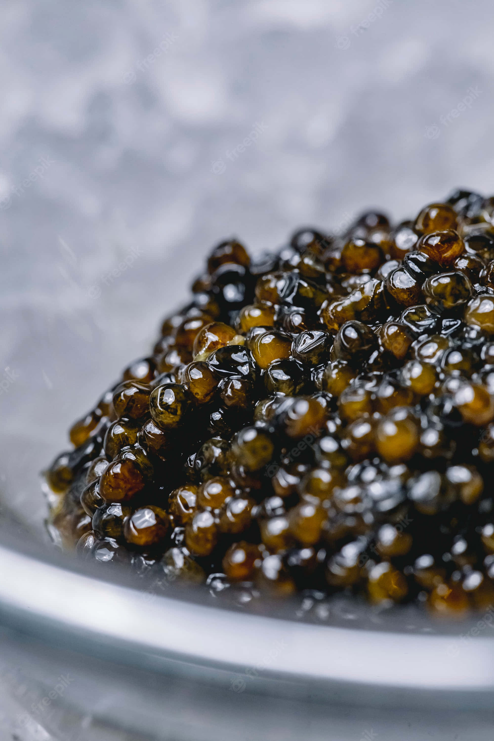 Black Caviar 桌布 壁紙 — 閃亮的黑色魚子醬珍珠堆放在透明玻璃碗中，背景為柔和的灰色紋理。
