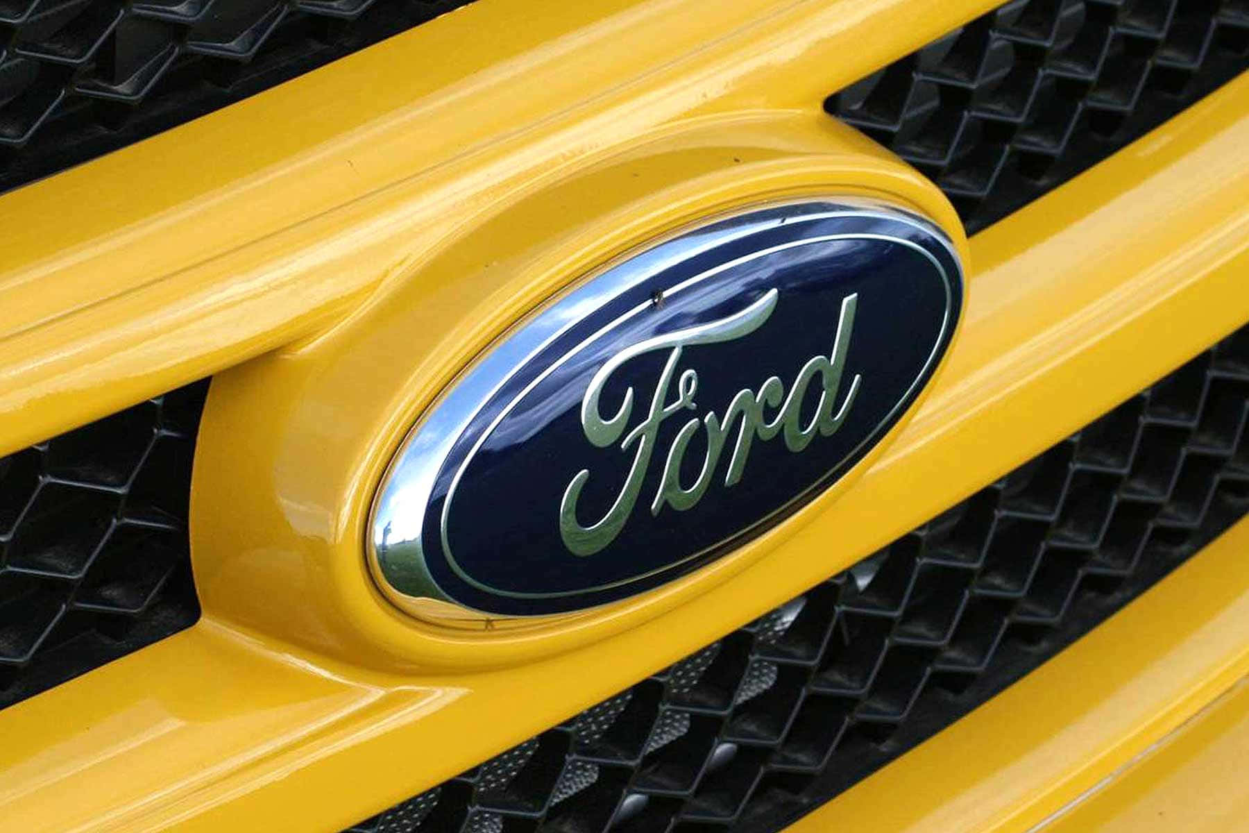 Ford Logo 桌布 壁紙 — 閃亮福特標誌的特寫，位於充滿活力的黃色汽車格柵上，帶有黑色網格背景。