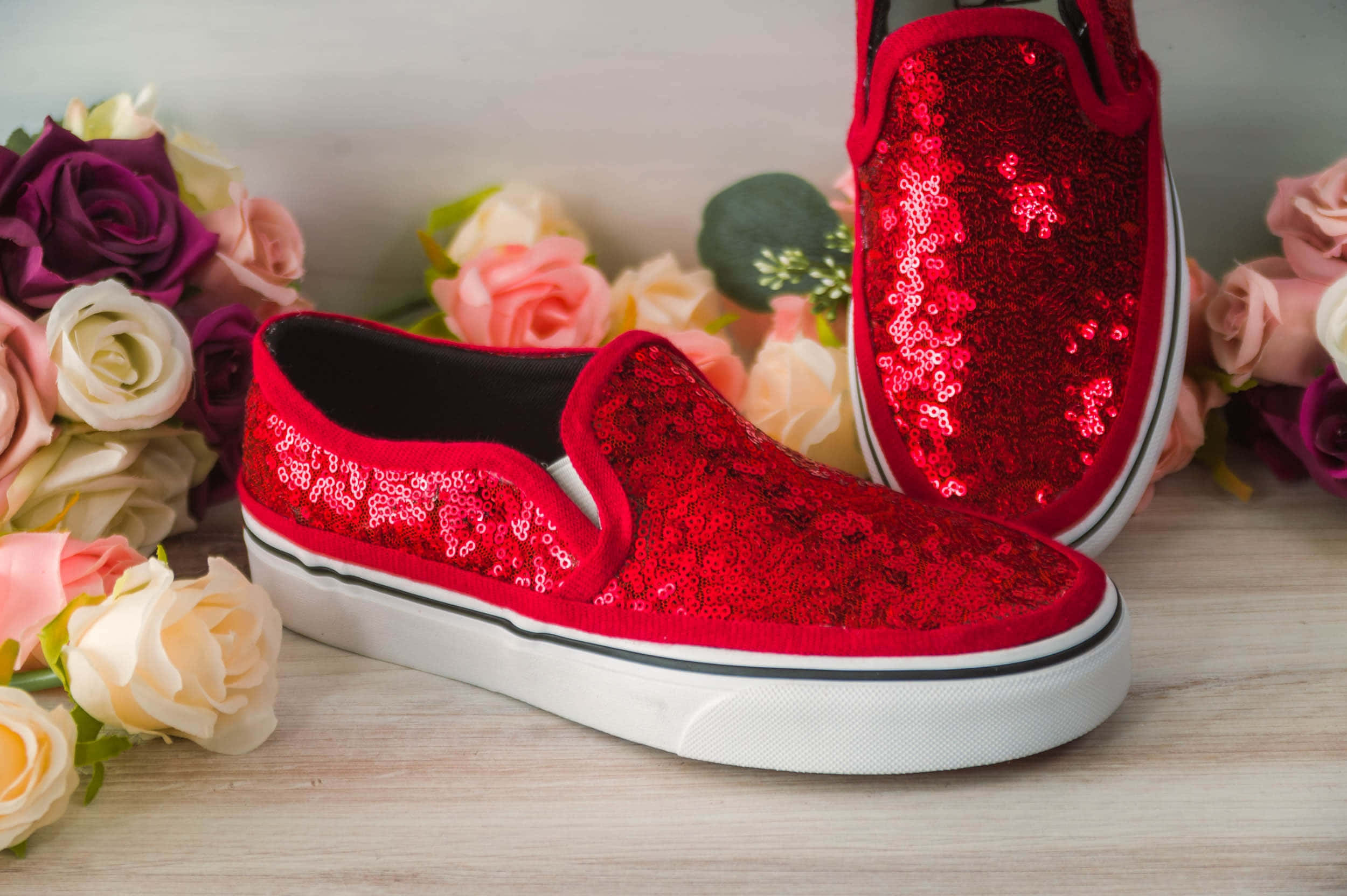 Red Shoes 桌布 壁紙 — 閃亮紅色亮片懶人運動鞋放置在木質表面上，周圍環繞著柔和的粉彩玫瑰。