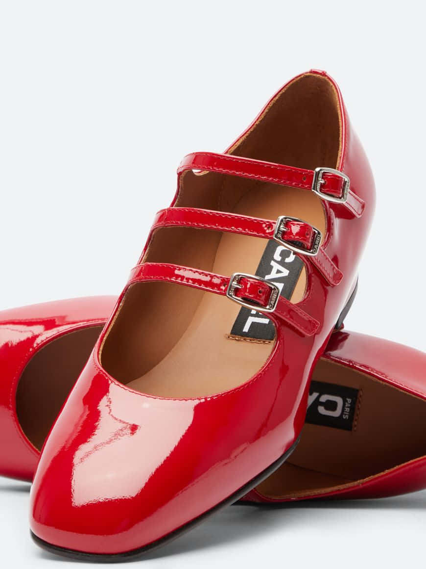 Red Shoes 桌布 壁紙 — 閃亮紅色漆皮瑪麗珍鞋，搭配銀色扣環和棕褐色內底，置於純白背景前。