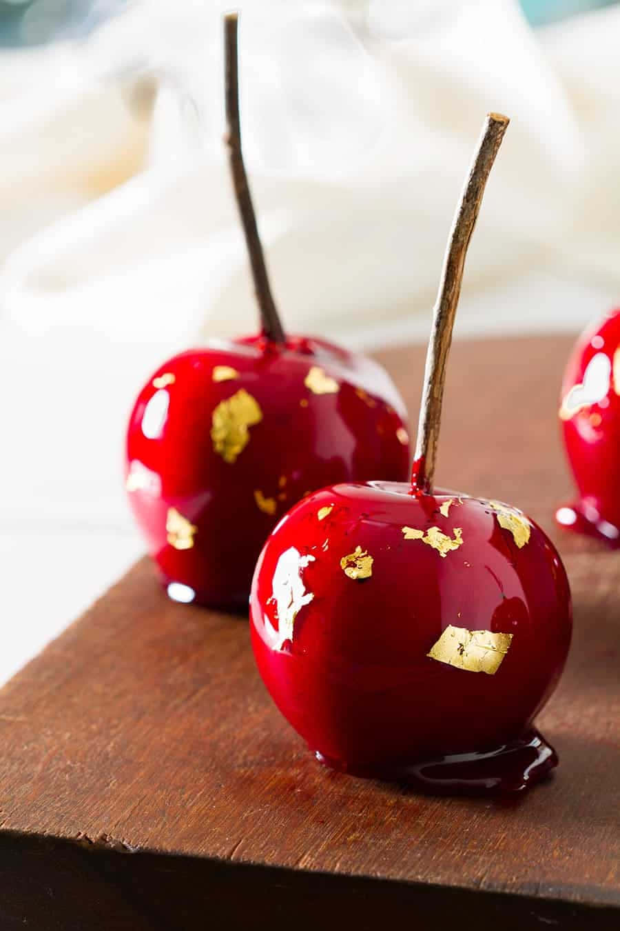 Candy Apples 桌布 壁紙 — 閃亮紅色糖蘋果飾以金箔，放在質樸的木質表面上。