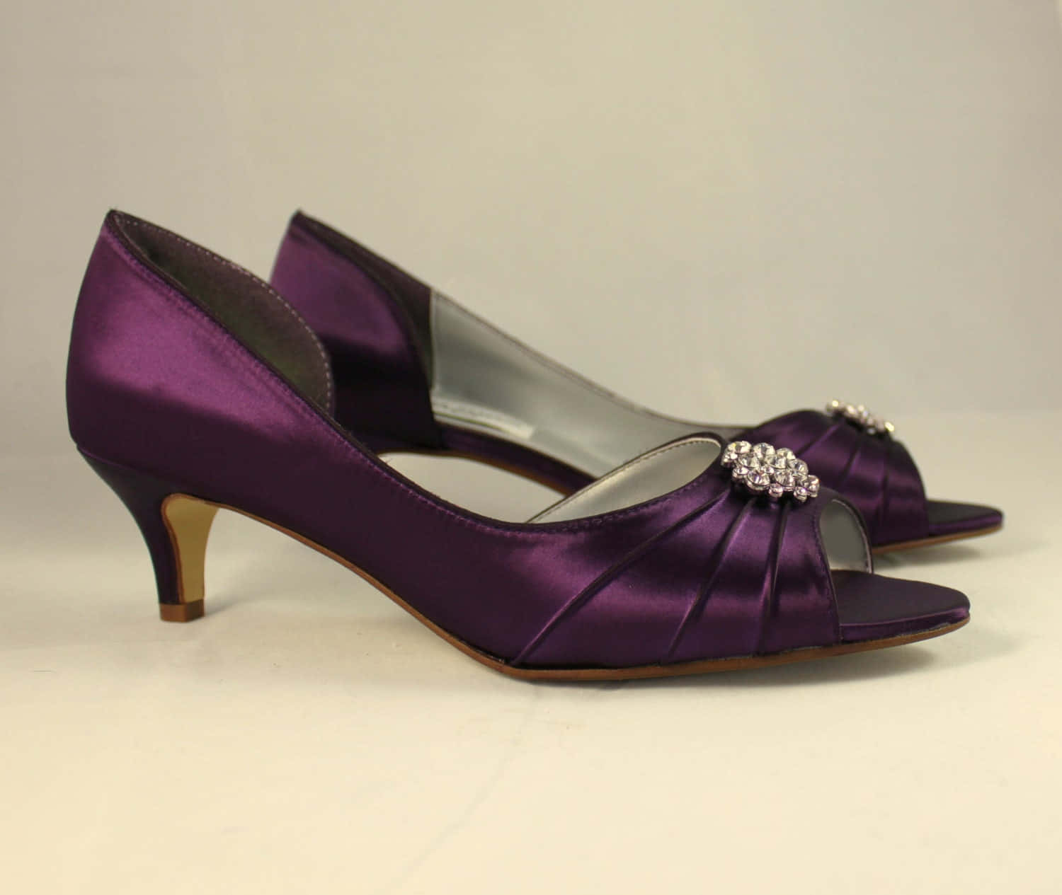 Purple Shoes 桌布 壁紙 — 閃亮紫色緞面魚口高跟鞋，飾有水晶裝飾和金色鞋跟，置於純白表面上。